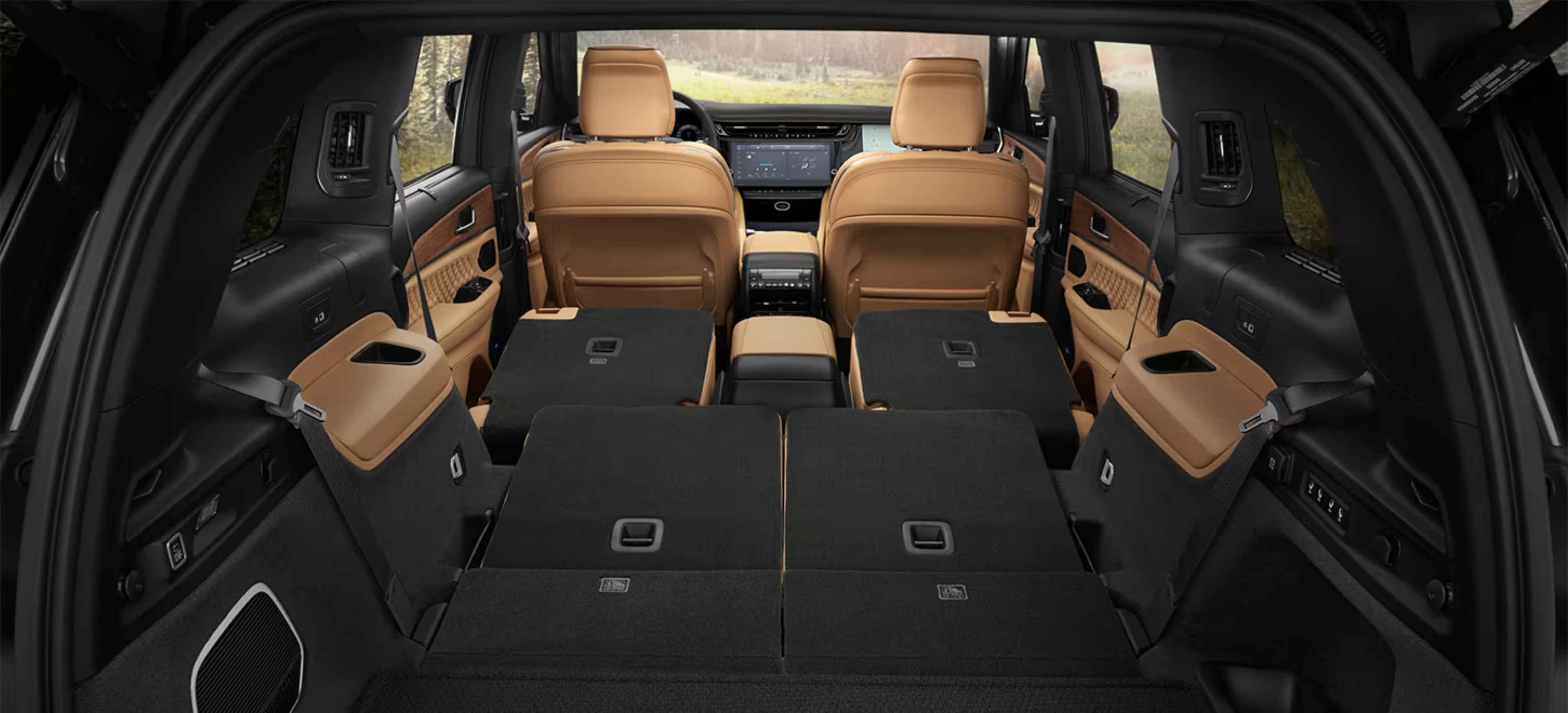 Interior of a vehicle with folded black and tan seats in the foreground and tan front seats and a dashboard in the background.