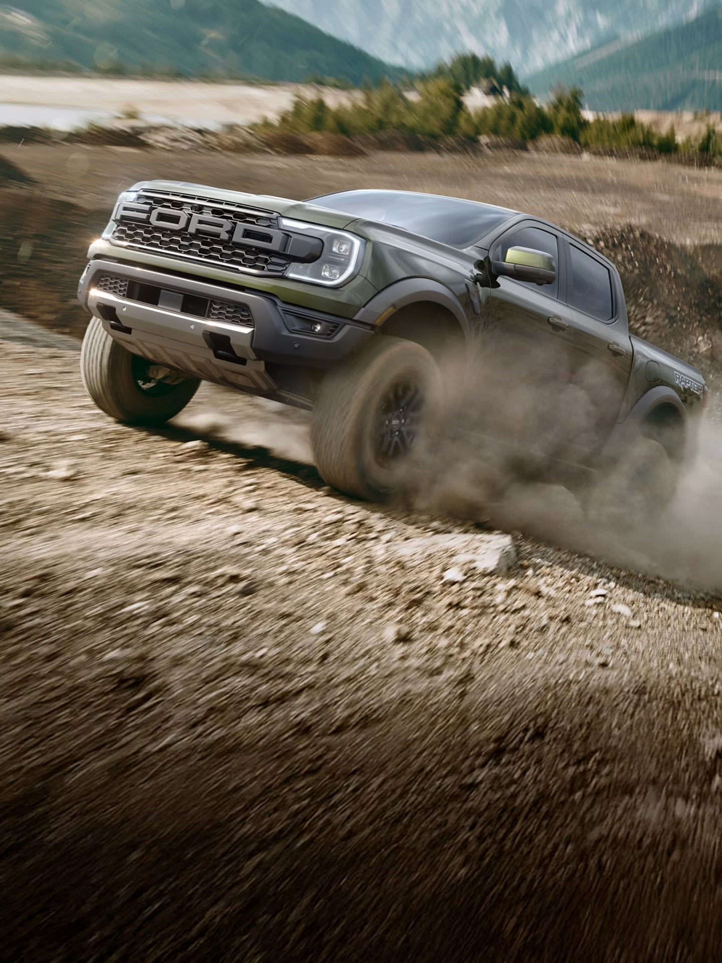 A dark green pickup truck kicks up dust as it navigates a steep, rocky incline, with blurred mountains in the background.