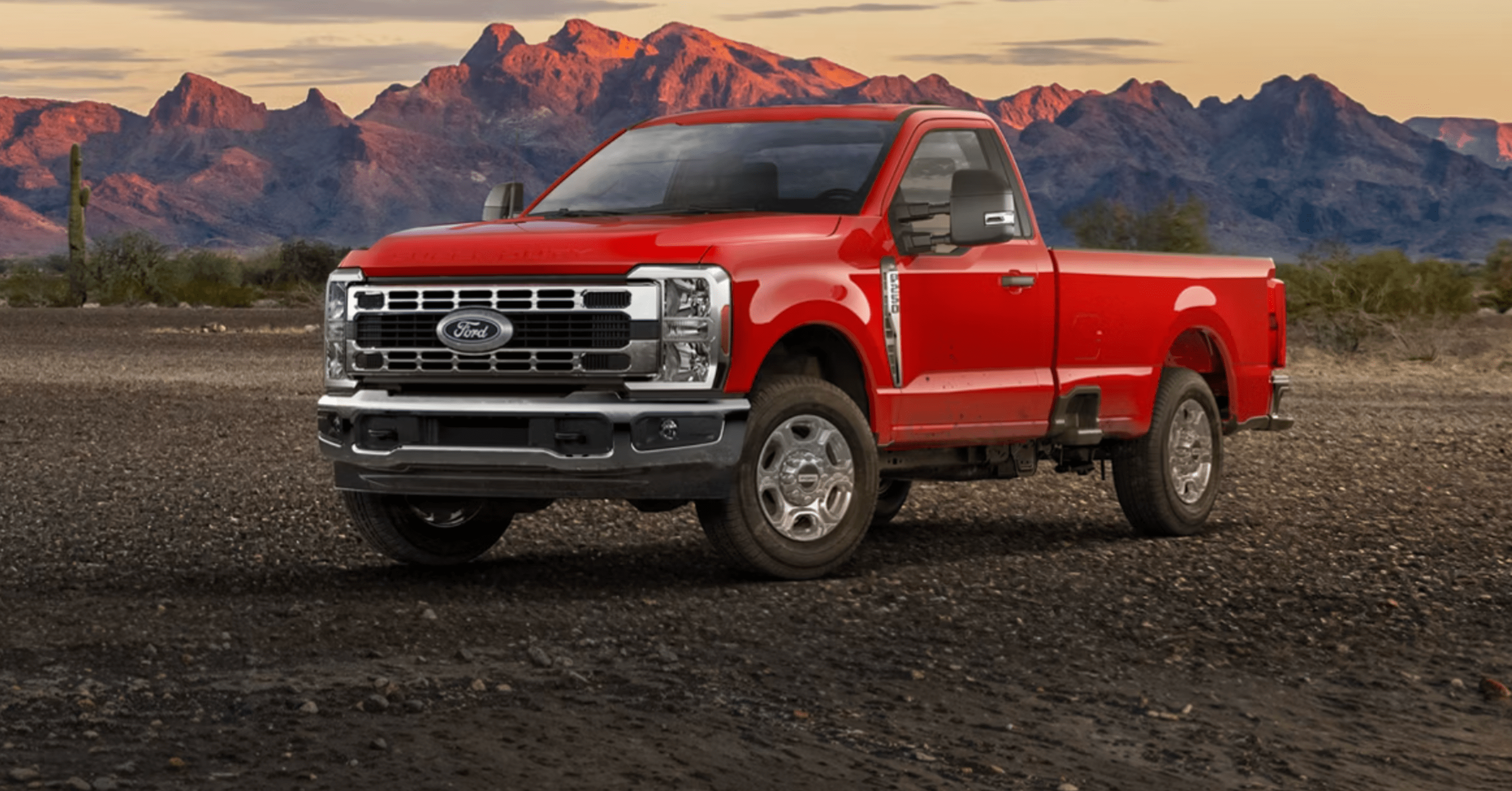 A red pickup truck on rocky terrain with sunlit mountains in the background.
