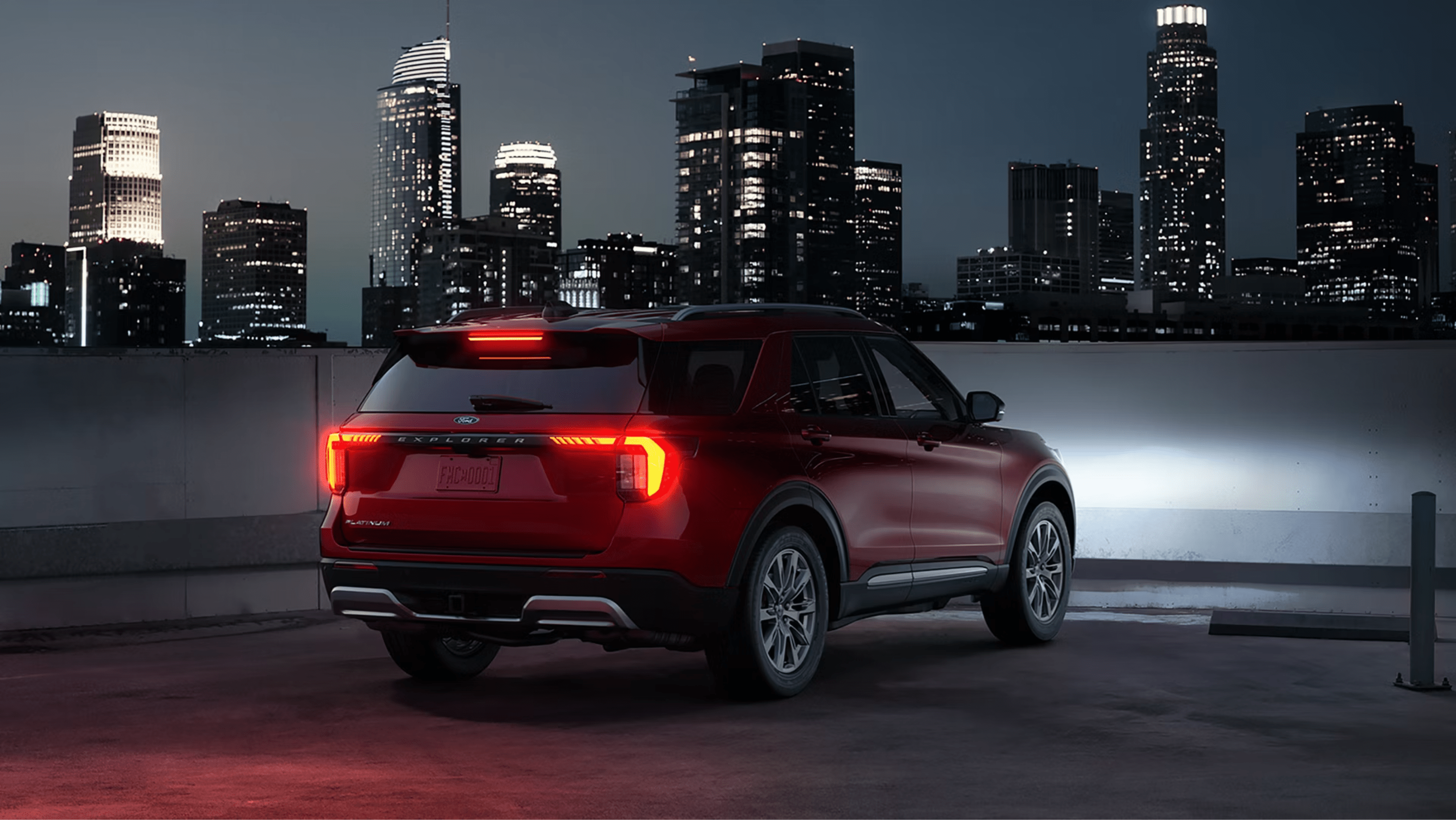 Red SUV parked on rooftop with city skyline at night