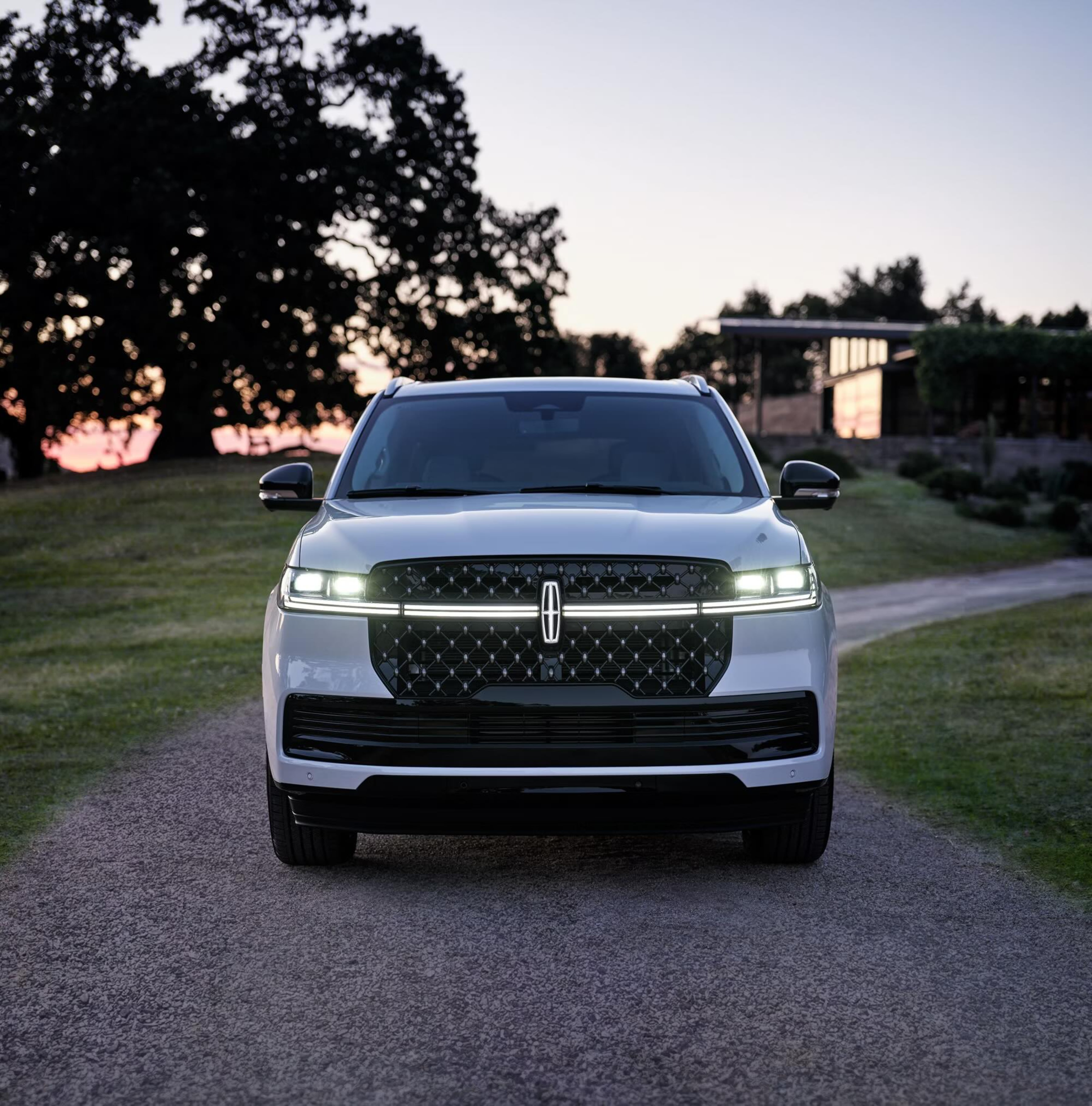 A white SUV parked on a gravel driveway in front of a modern house with trees in the background.