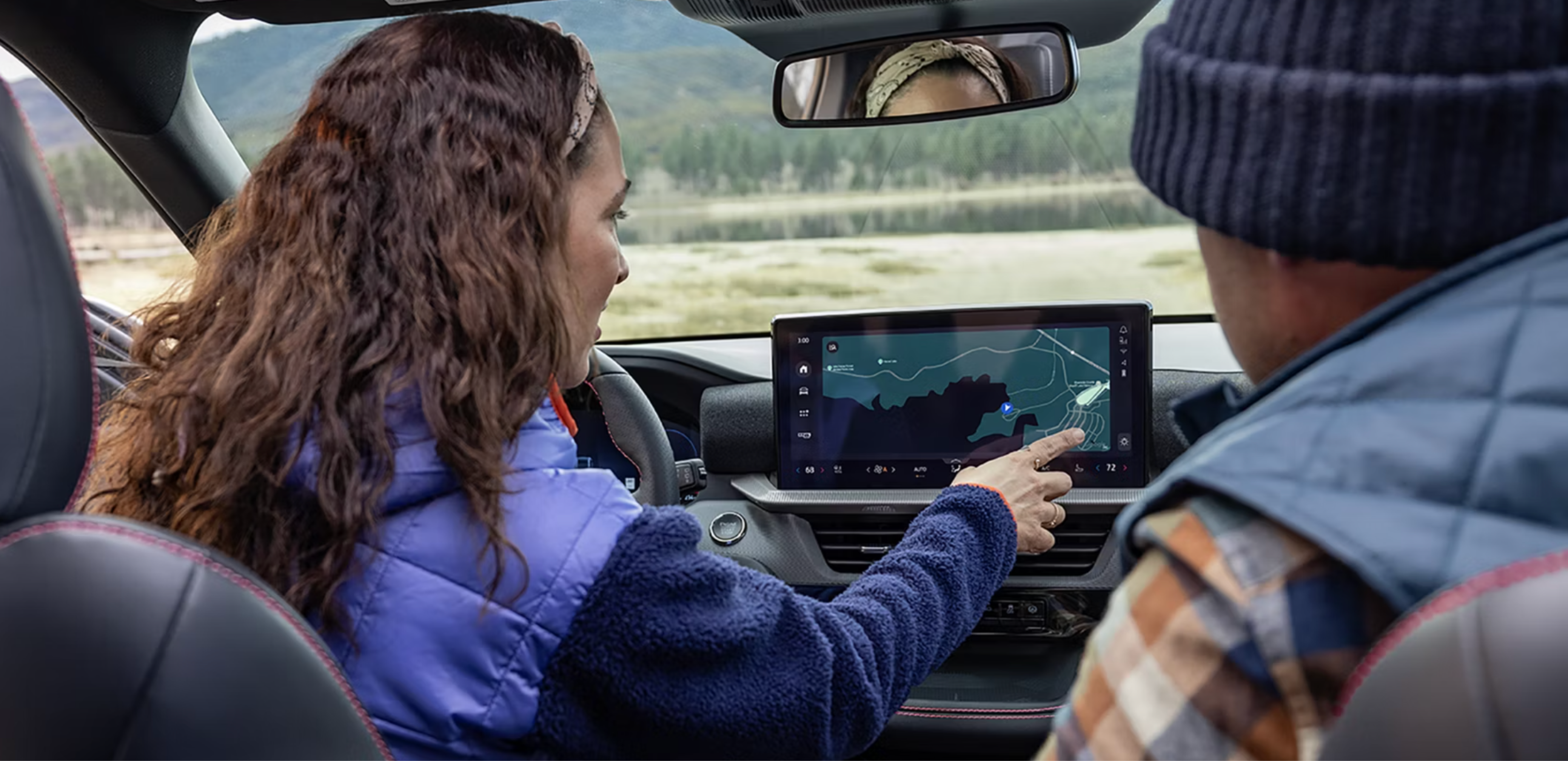 A person interacting with a car navigation system displaying a scenic landscape through the windshield.