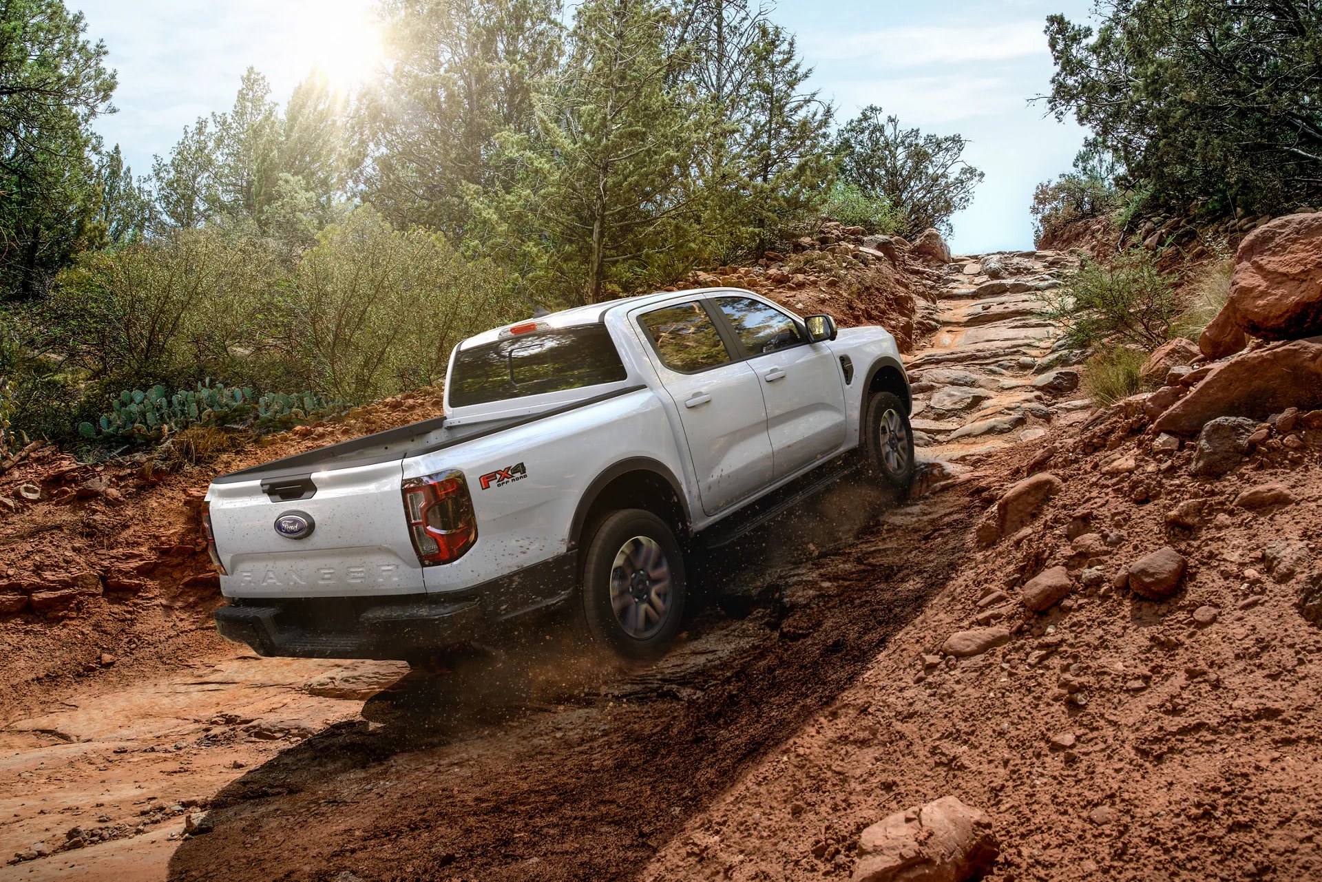 A white pickup truck navigating a rugged, dirt trail surrounded by lush greenery and towering rock formations in the background.