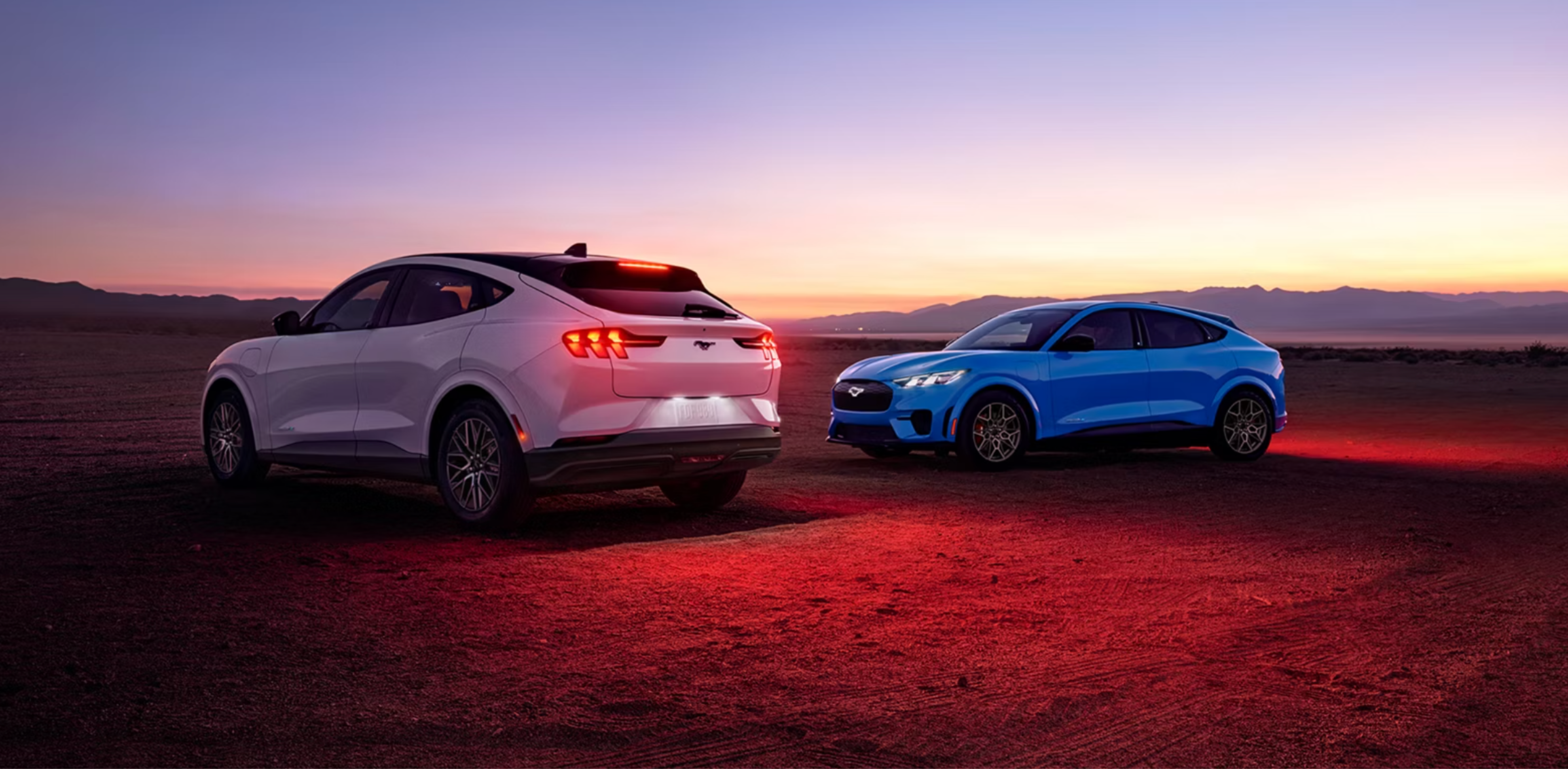 Two SUVs, one white and one blue, are parked on a dusty plain under a twilight sky with distant mountains.
