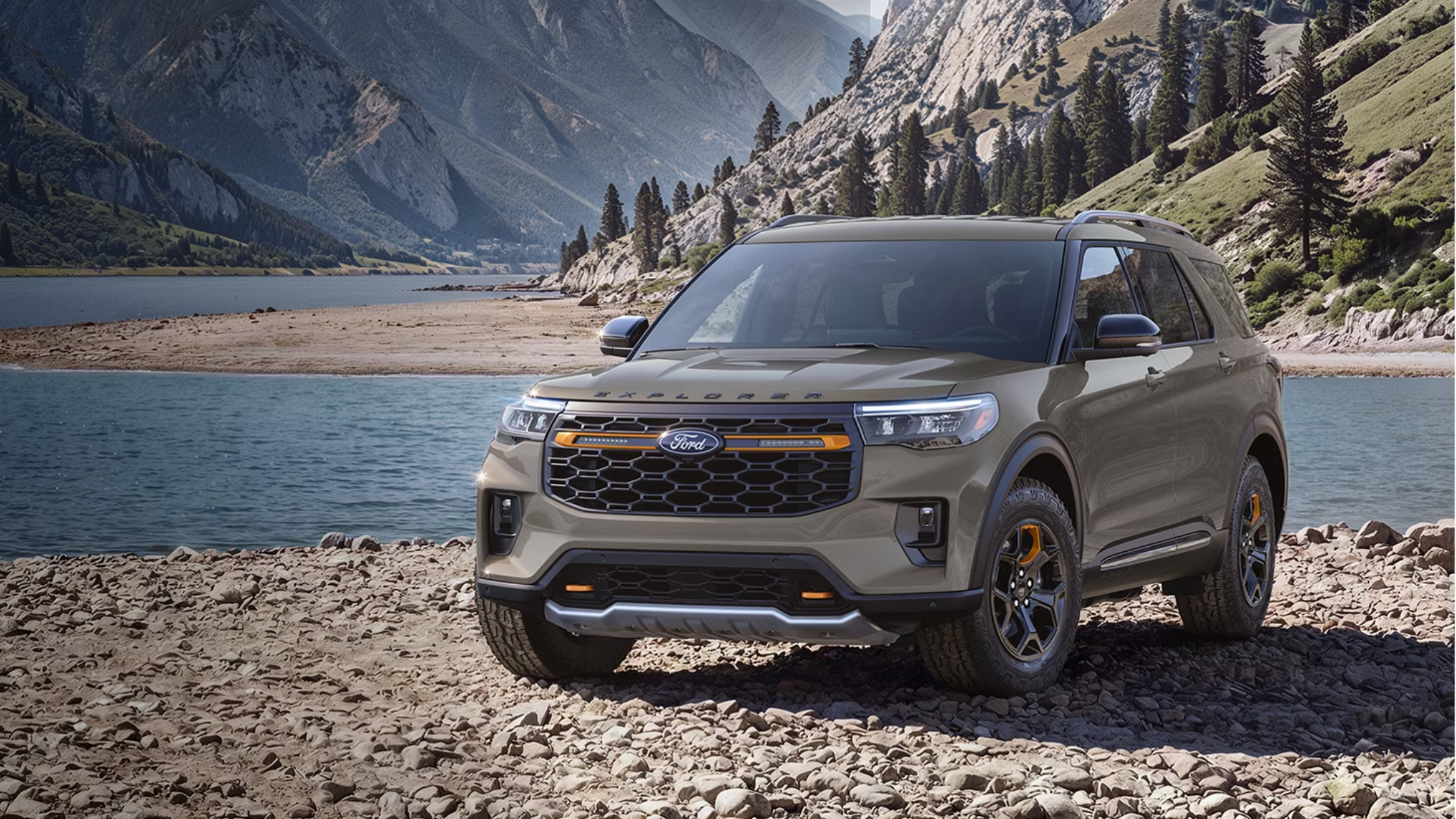 A tan SUV is parked on a rocky shoreline with a calm lake and rugged mountains in the background.