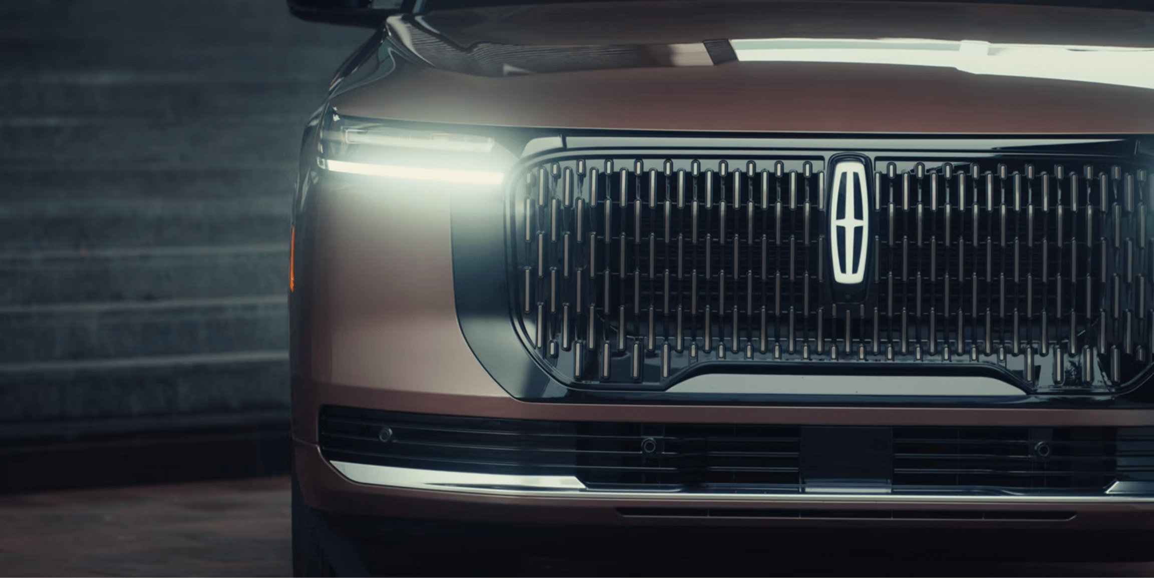 Brown vehicle front grille and headlight against stone steps background.