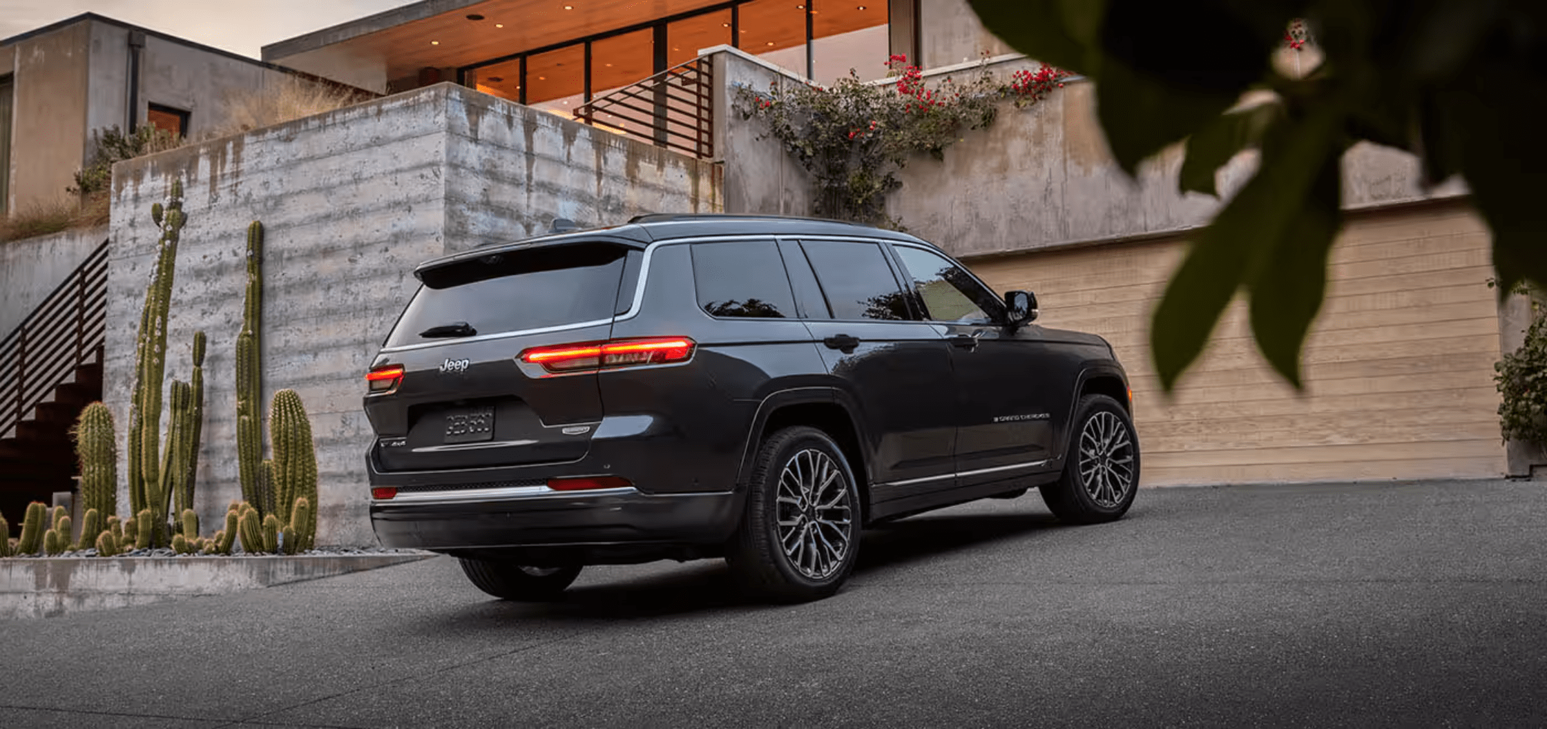 A dark grey SUV is parked on a driveway in front of a modern house with cacti and greenery.