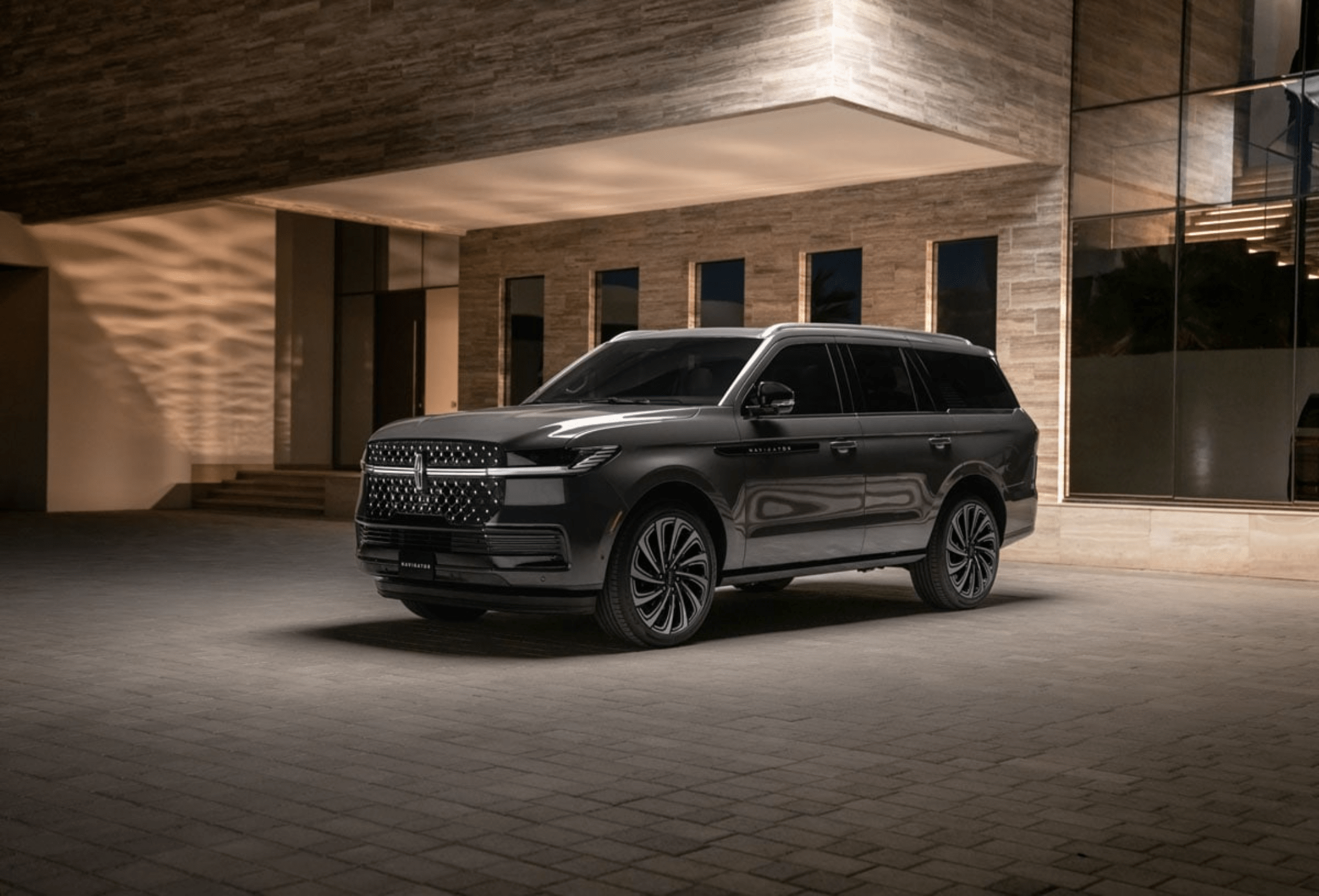 A dark gray SUV is parked on a paved surface in front of a modern building with large windows and textured walls.