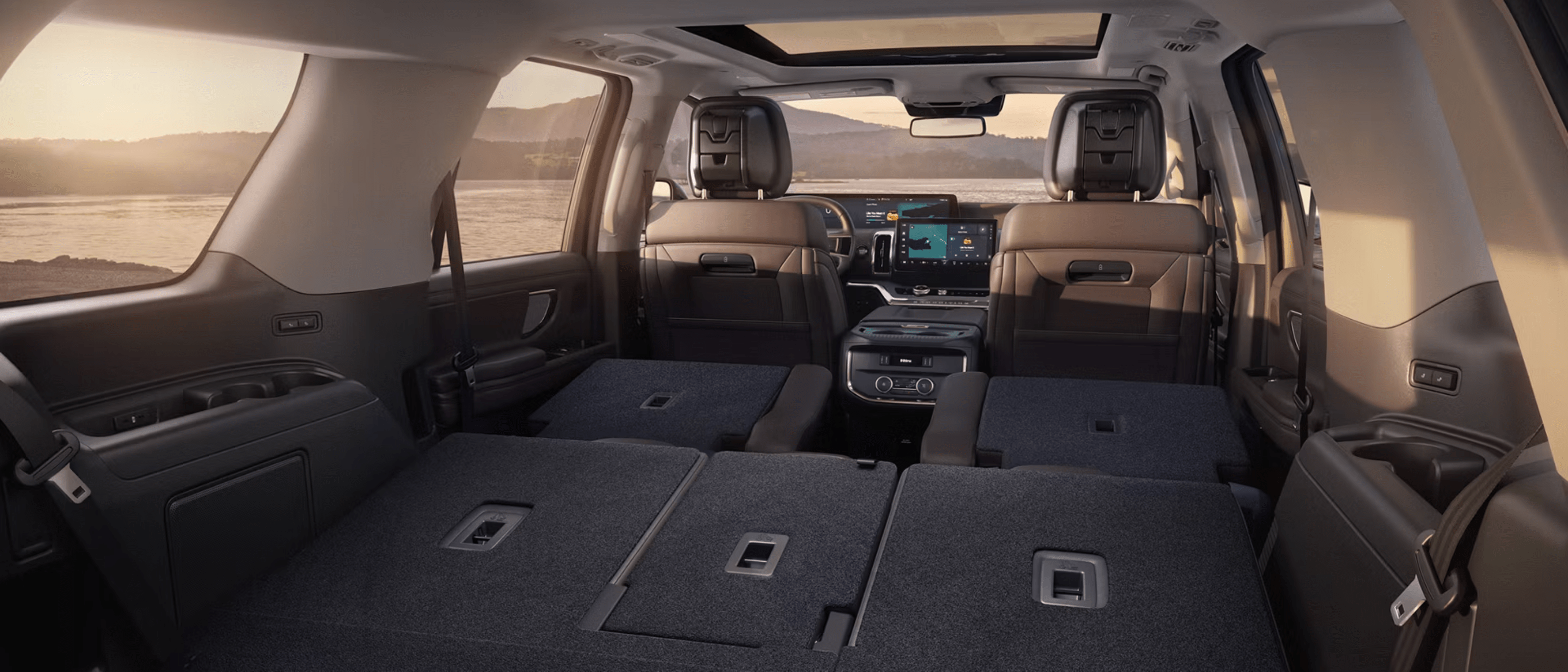 Interior of a modern SUV with folded rear seats and panoramic sunroof overlooking a coastal landscape.