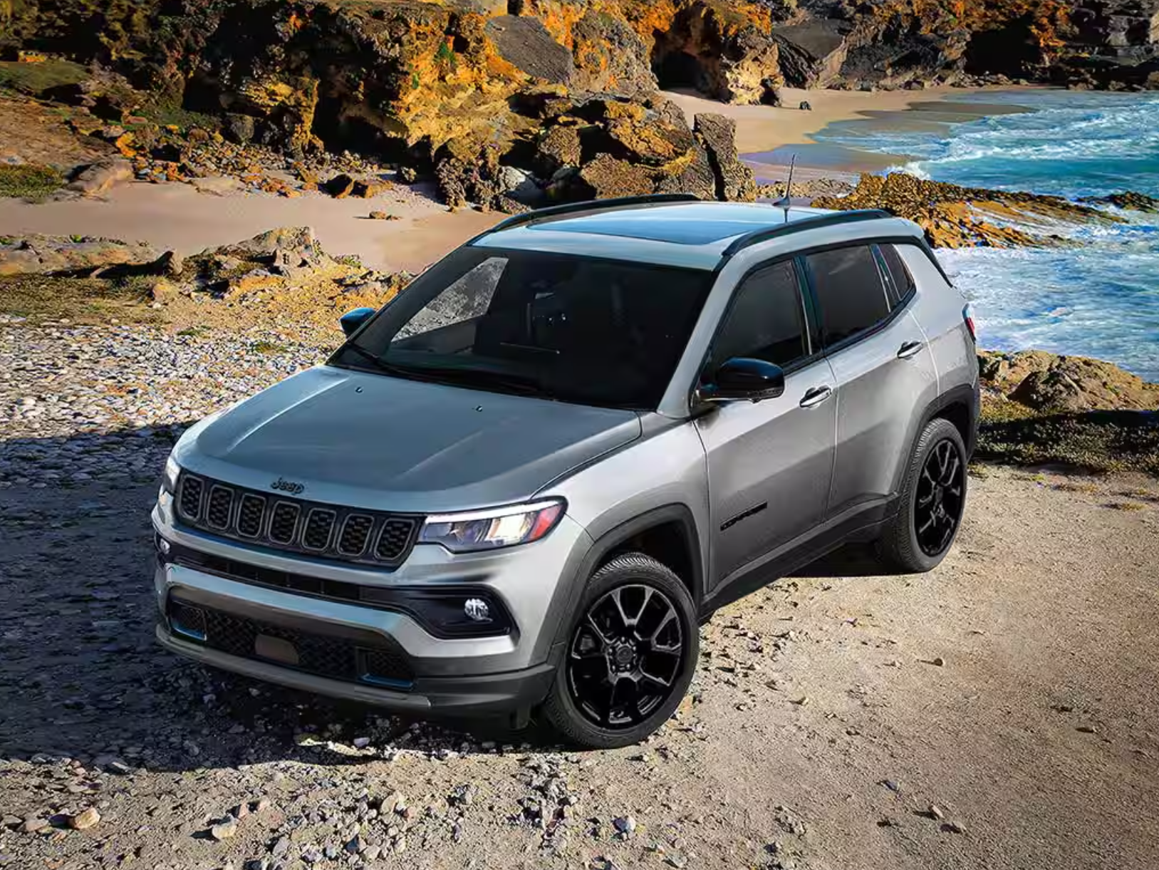 A silver SUV parked on a rocky shoreline with ocean waves in the background.