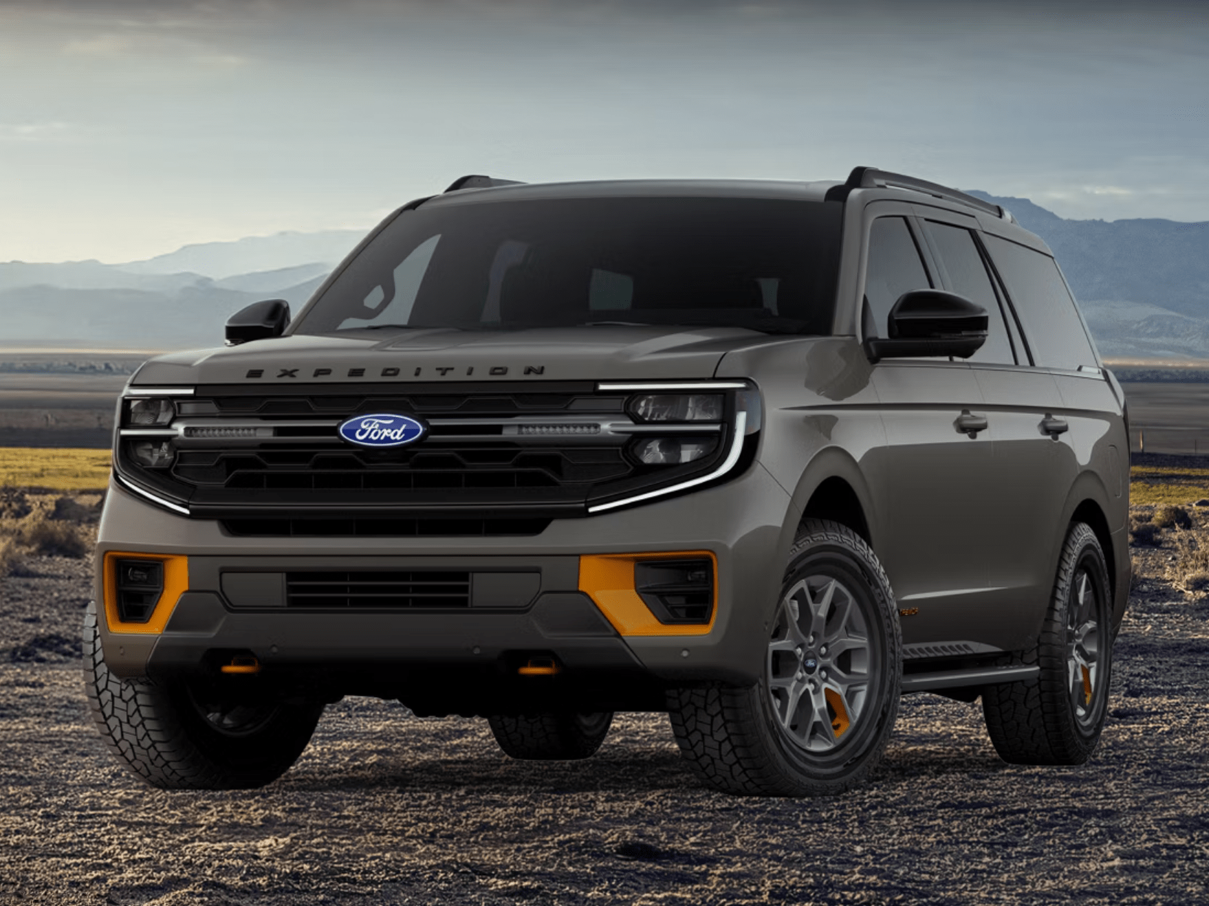 A grey SUV parked on desert terrain with mountains in the background.