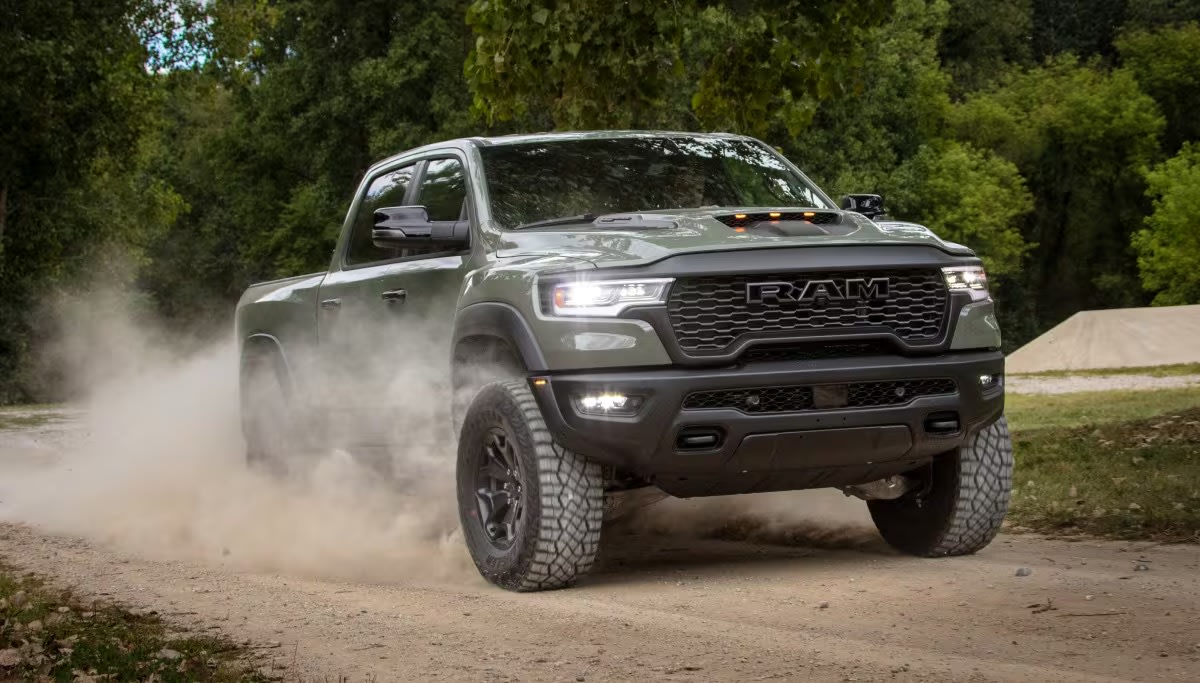 A green pickup truck kicks up a cloud of dust on a dirt path against a backdrop of lush green trees.