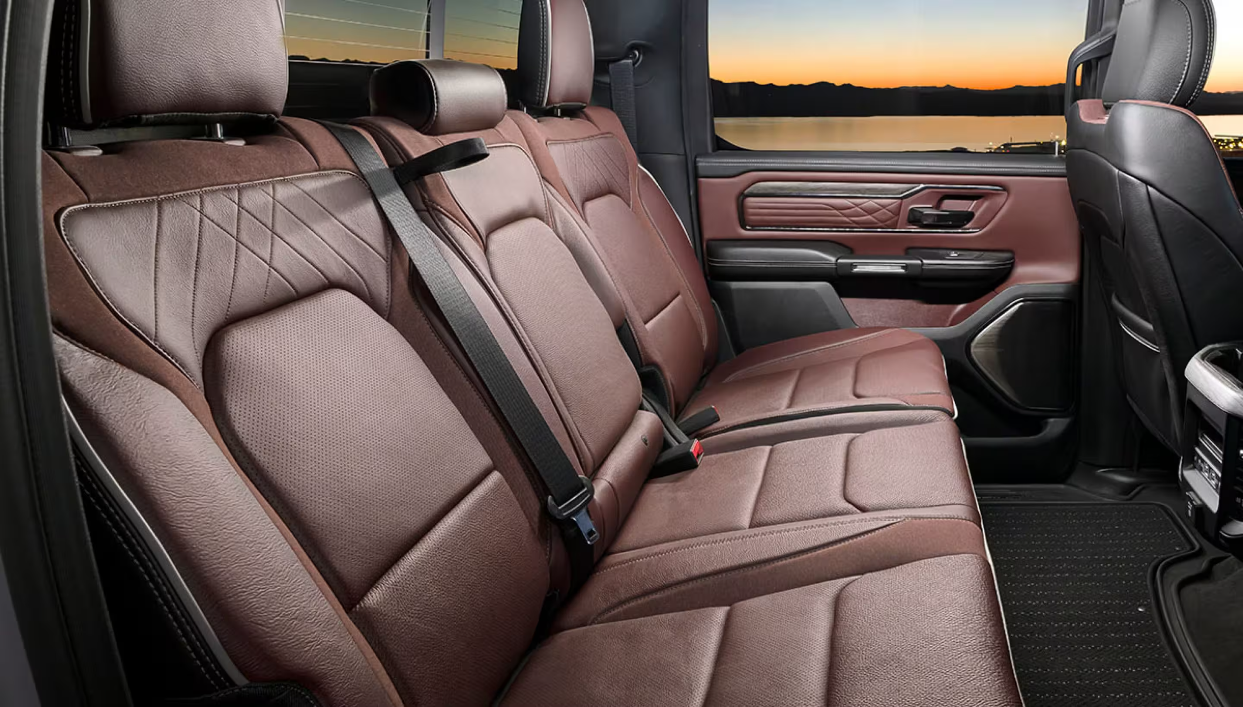 Brown leather rear seats in a vehicle interior with a sunset over a lake visible through the window.