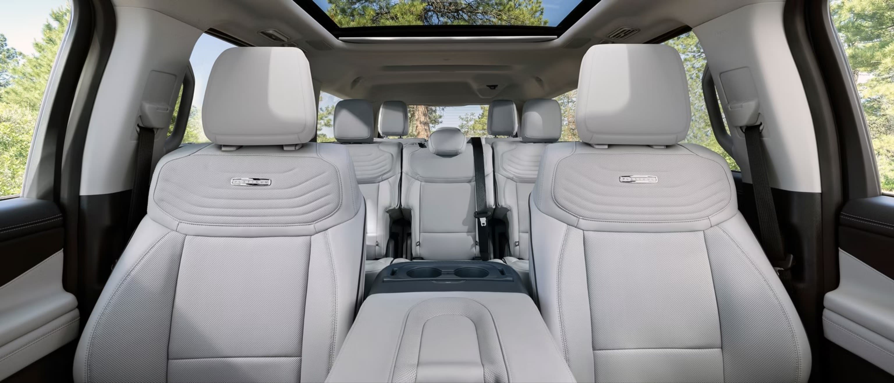Light gray leather car seats and a panoramic sunroof showcasing green trees.