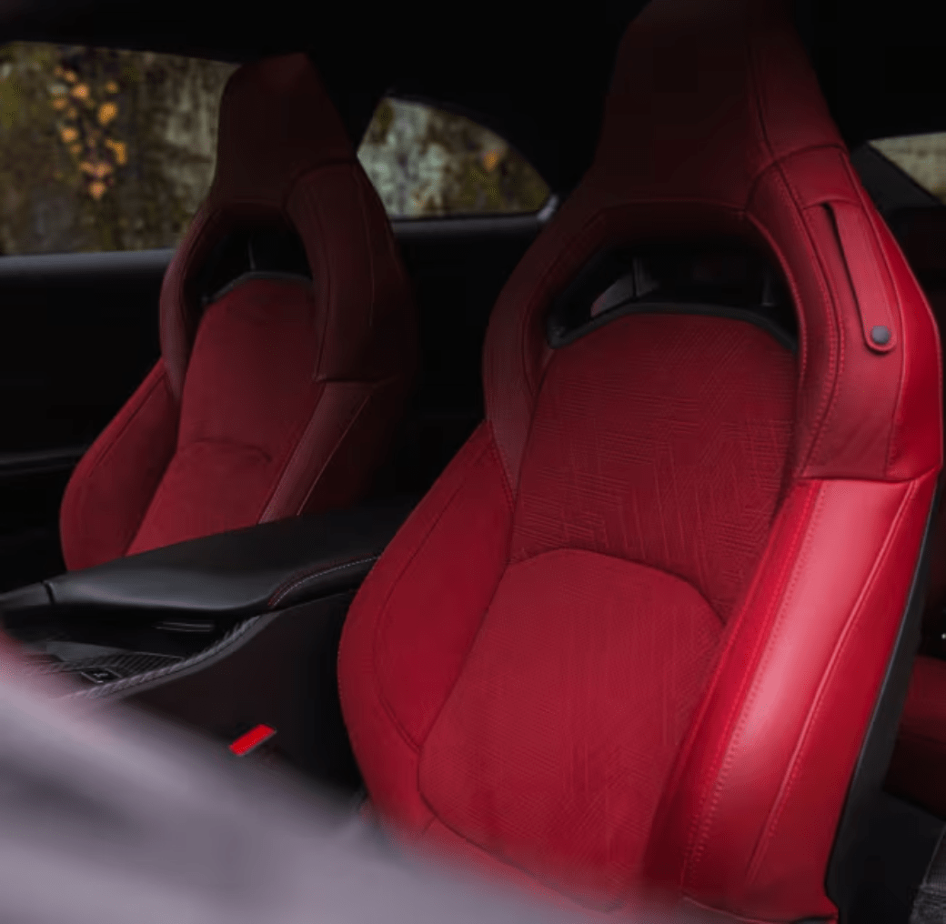 Two red racing seats in a car interior with a blurred outdoor landscape visible through the window.