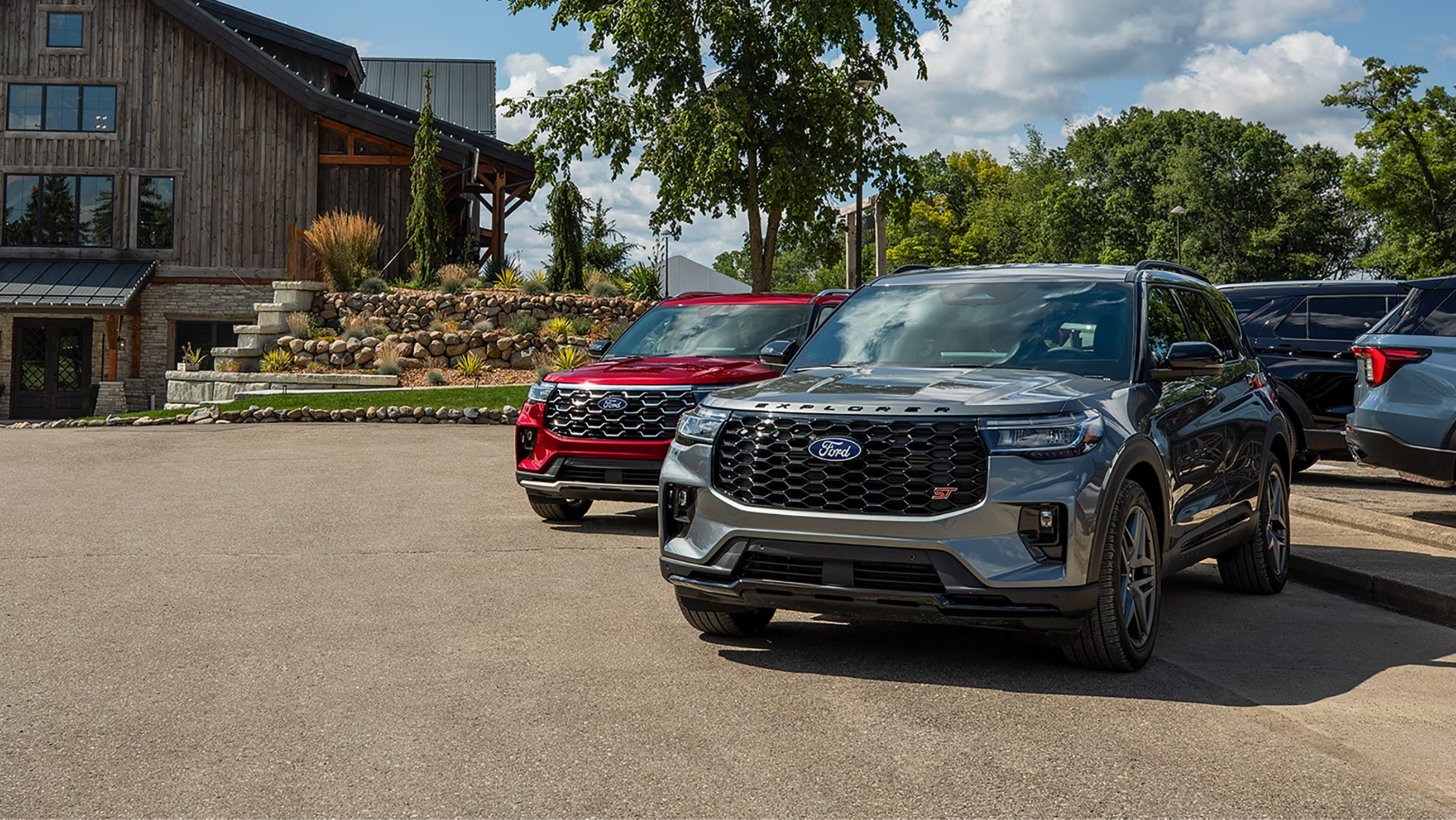 Two SUVs are parked in front of a wooden building and trees.