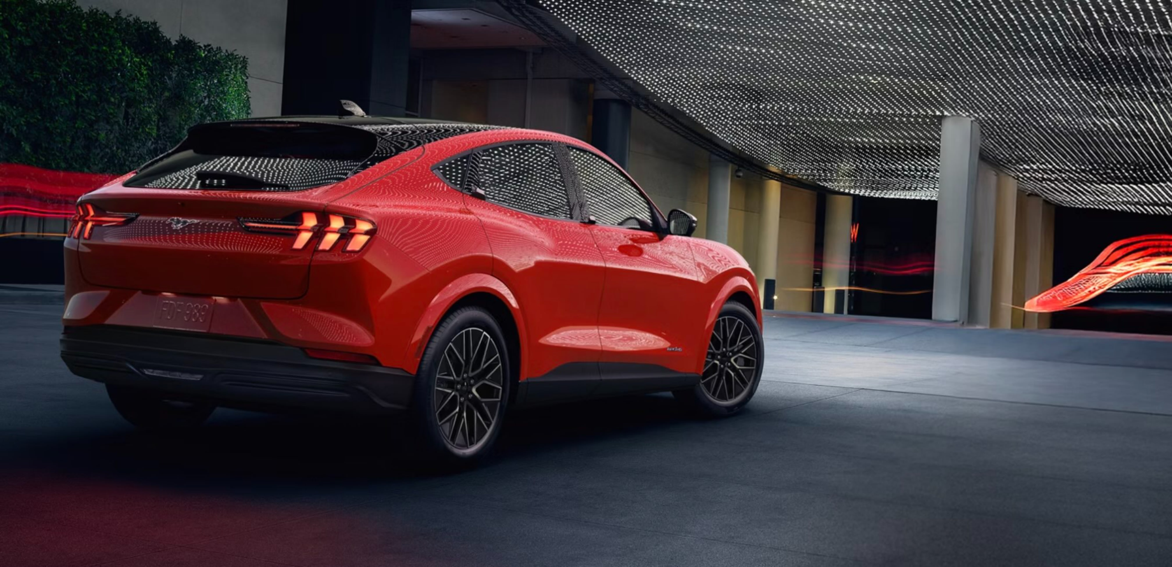 A red car parked in a modern garage with a textured ceiling and abstract art in the background.