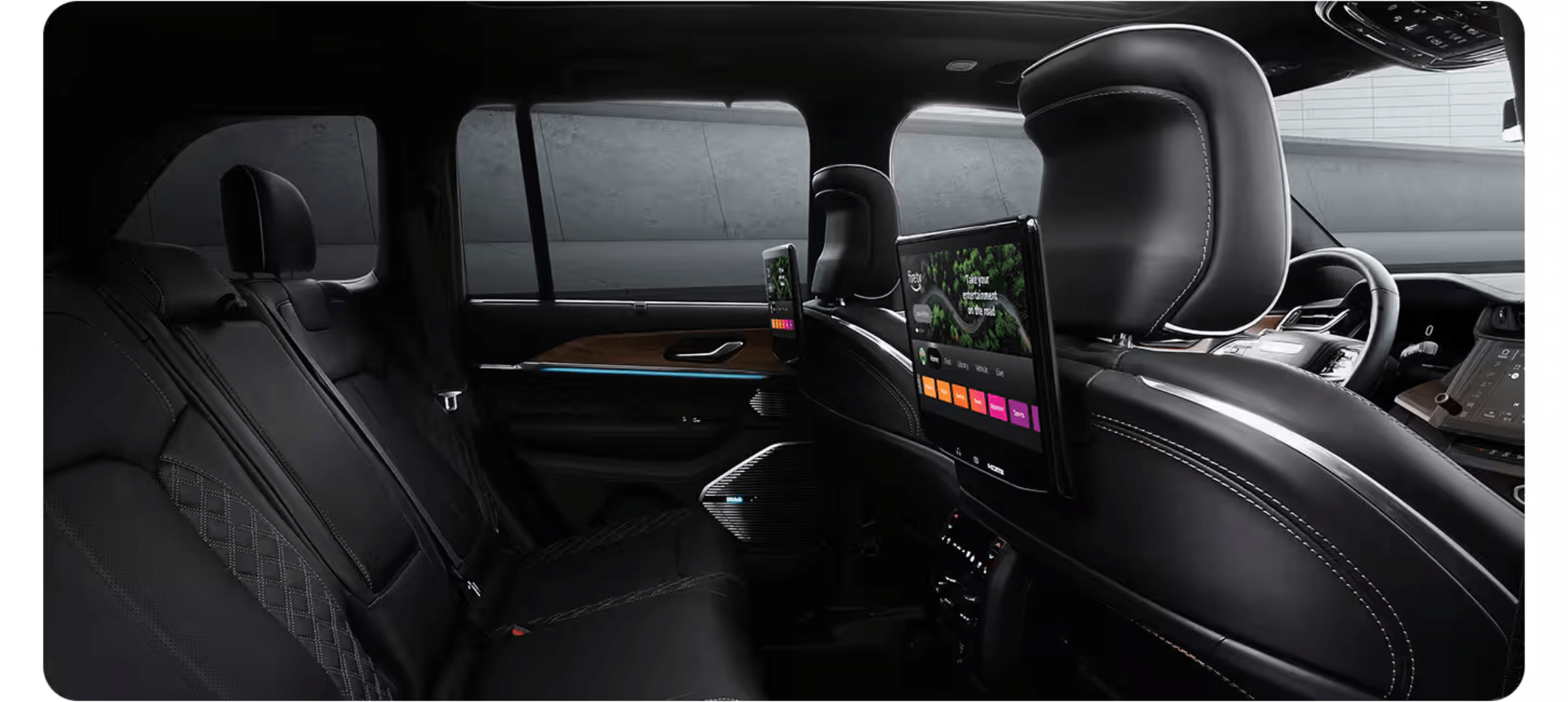 Black leather car seats with integrated entertainment screens in the foreground, with a blurred concrete wall visible through the windows in the background.