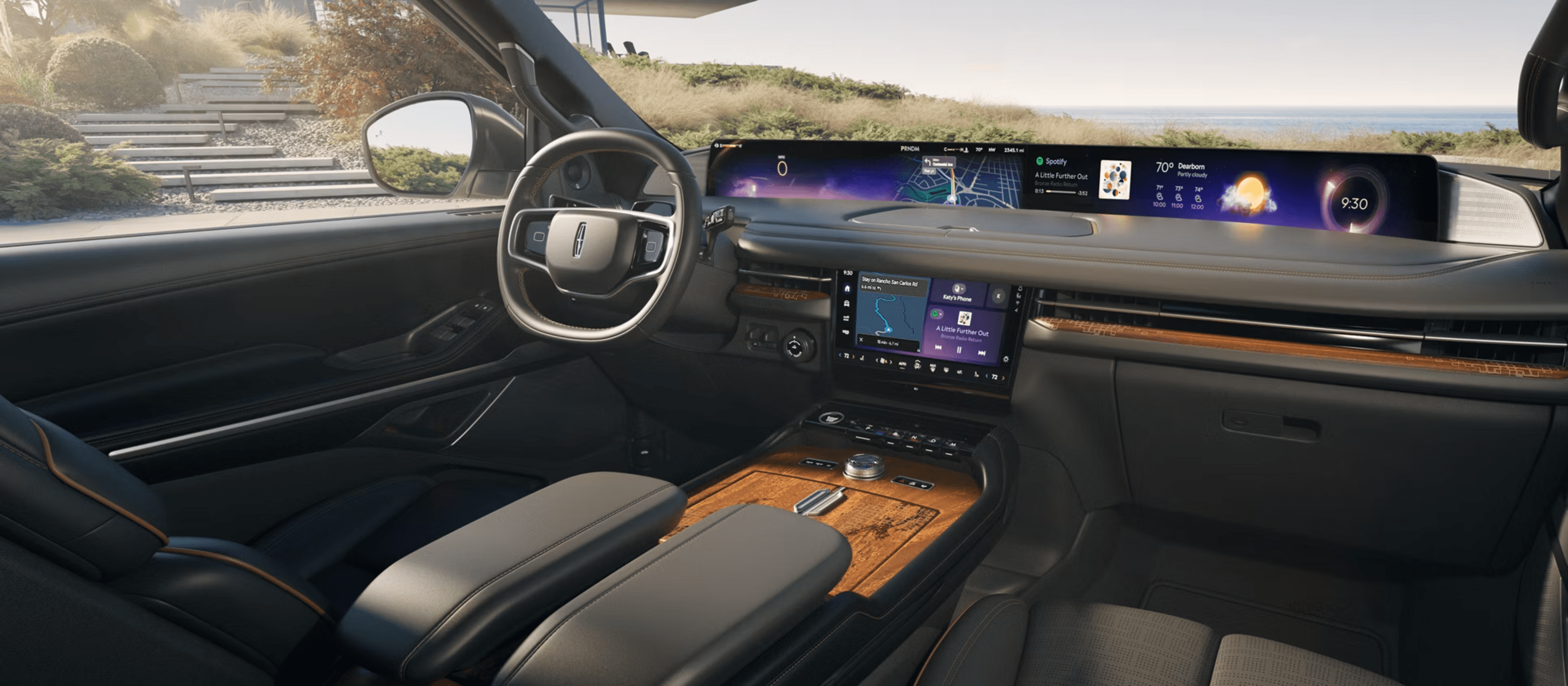Modern vehicle interior with a wide digital dashboard, leather seats, and a scenic coastal landscape visible through the windows.