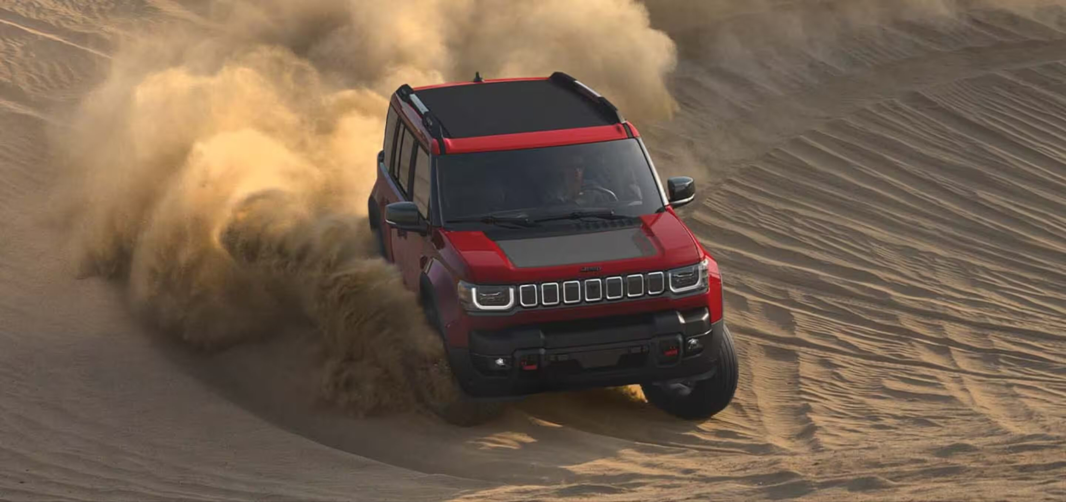 A red SUV kicks up a large cloud of sand as it drives across a desert dune.