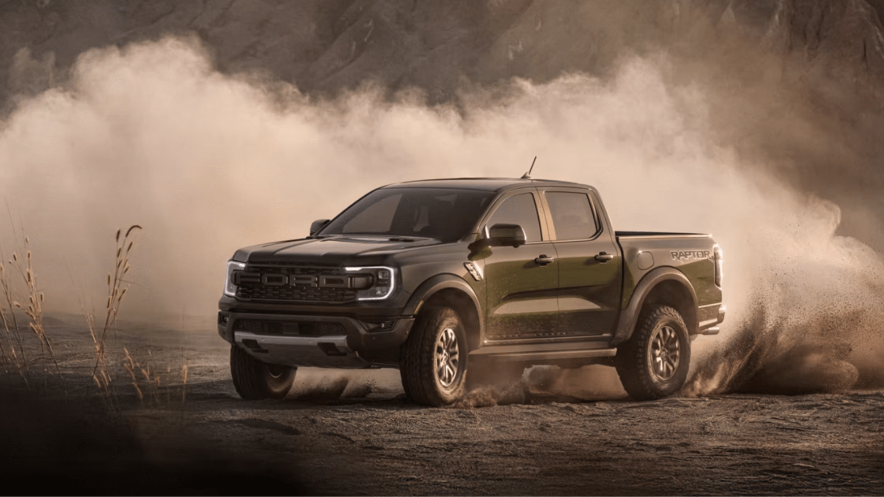 A dark green pickup truck kicks up a massive cloud of dust while driving across a rugged desert landscape.