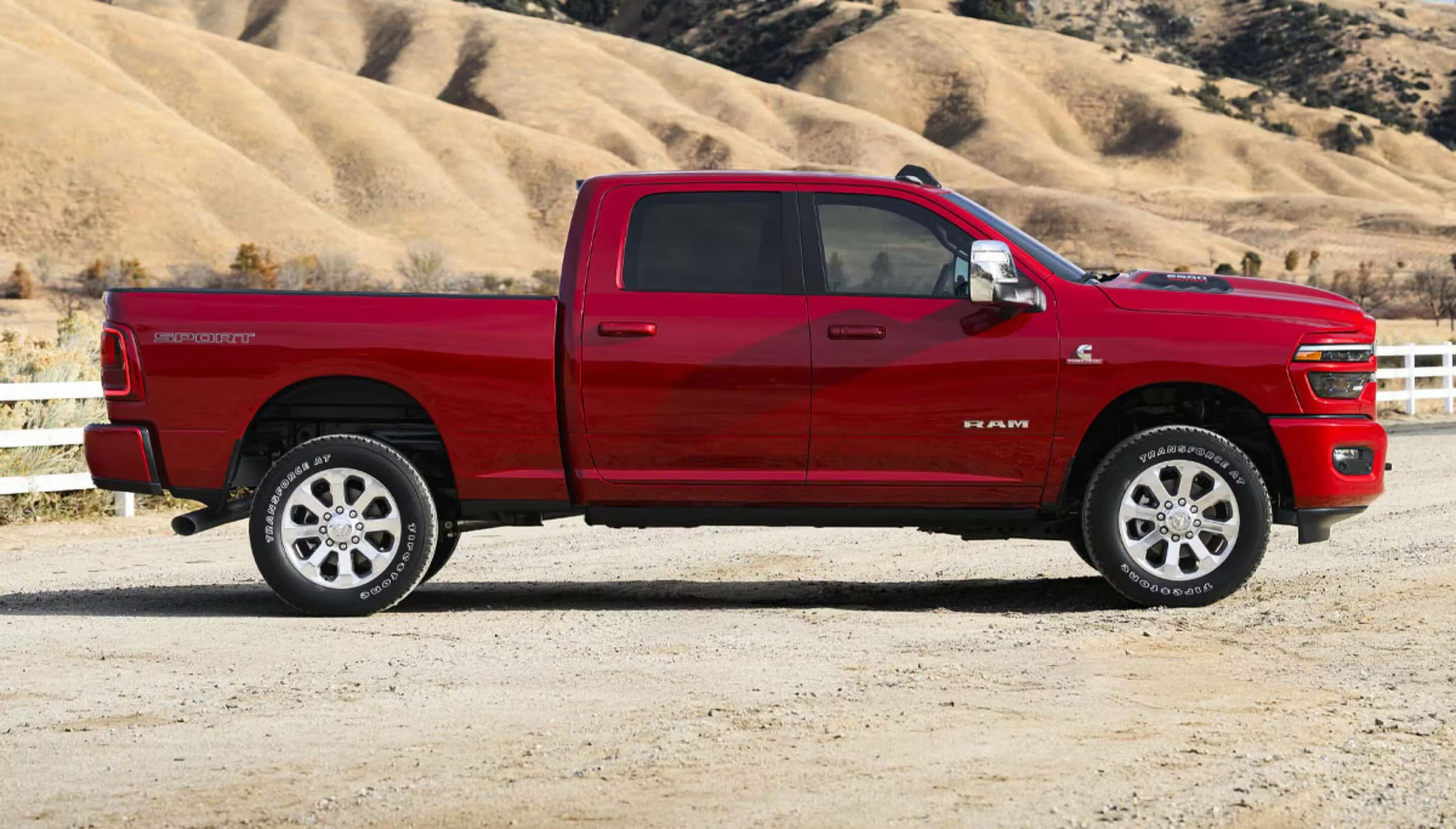 A red pickup truck parked on a dirt road with rolling hills in the background.