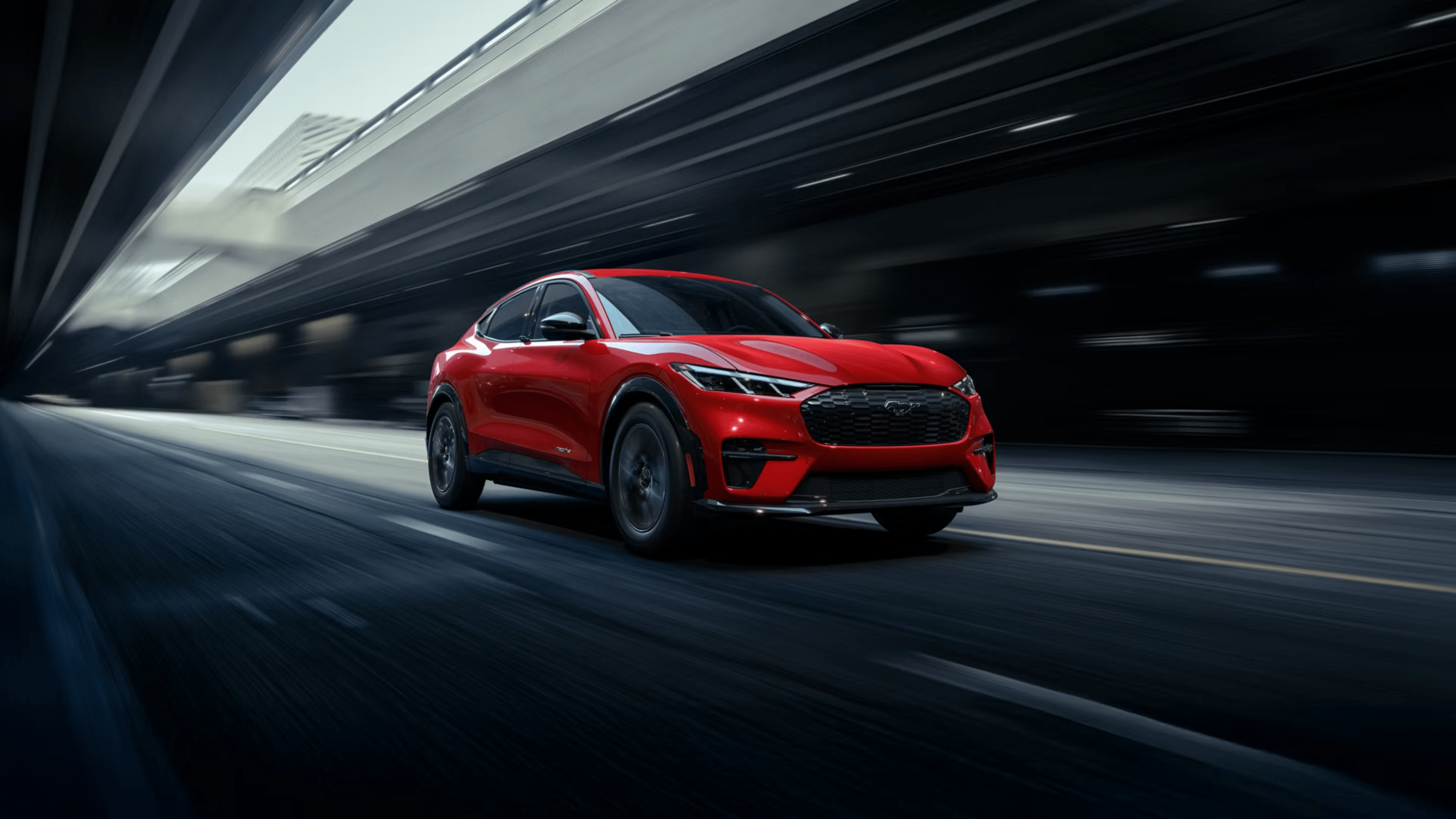 A red electric sports car speeds through a dark, modern tunnel with blurred concrete walls.