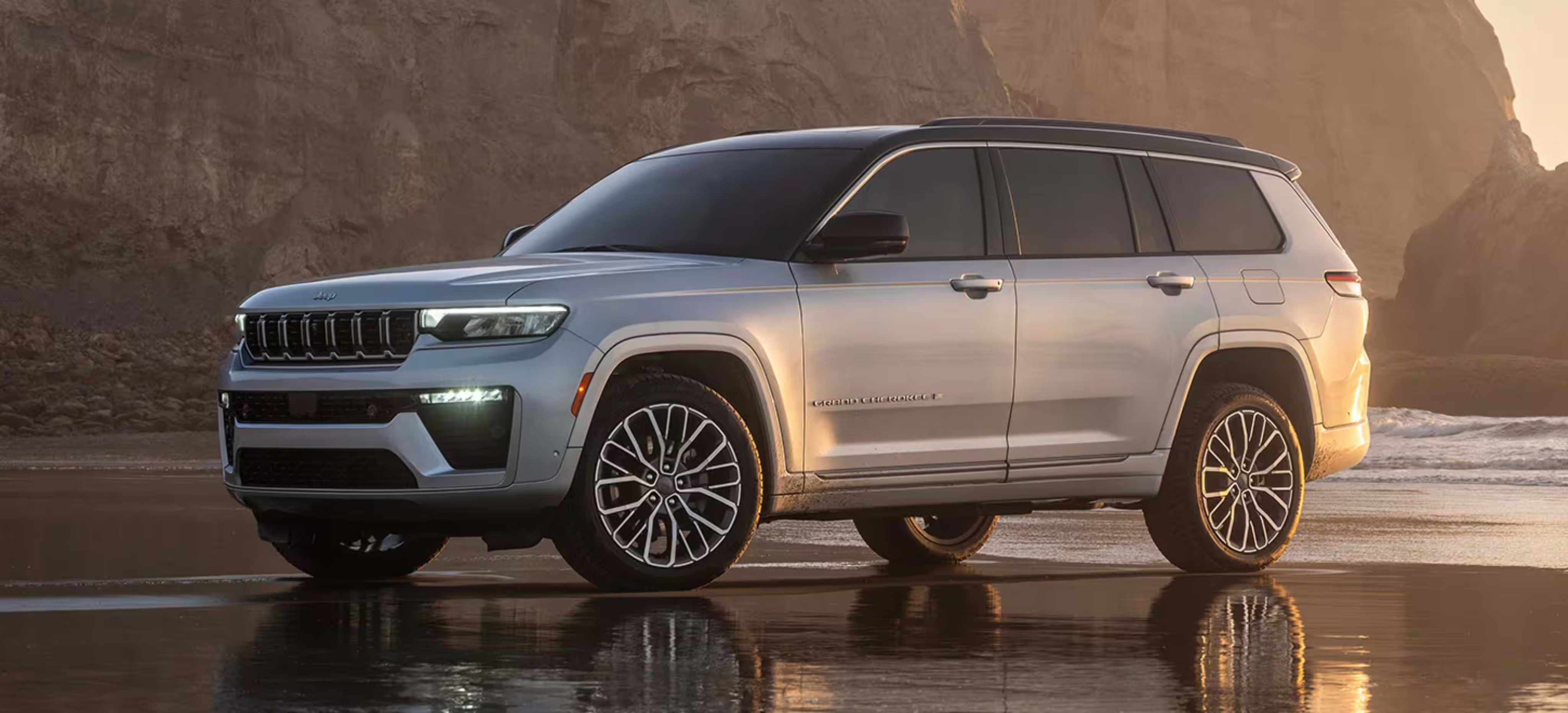 Silver SUV parked on wet sandy beach with cliffs in the background