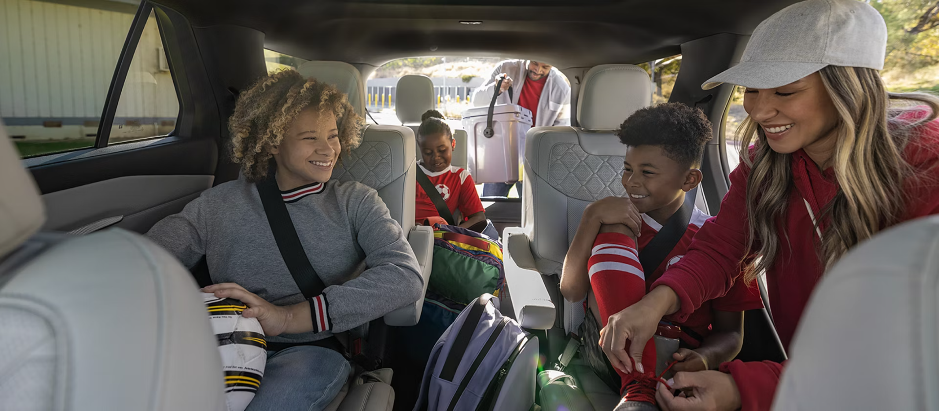 A woman helping a young boy with his seatbelt in a car, with a girl and a man in the background.