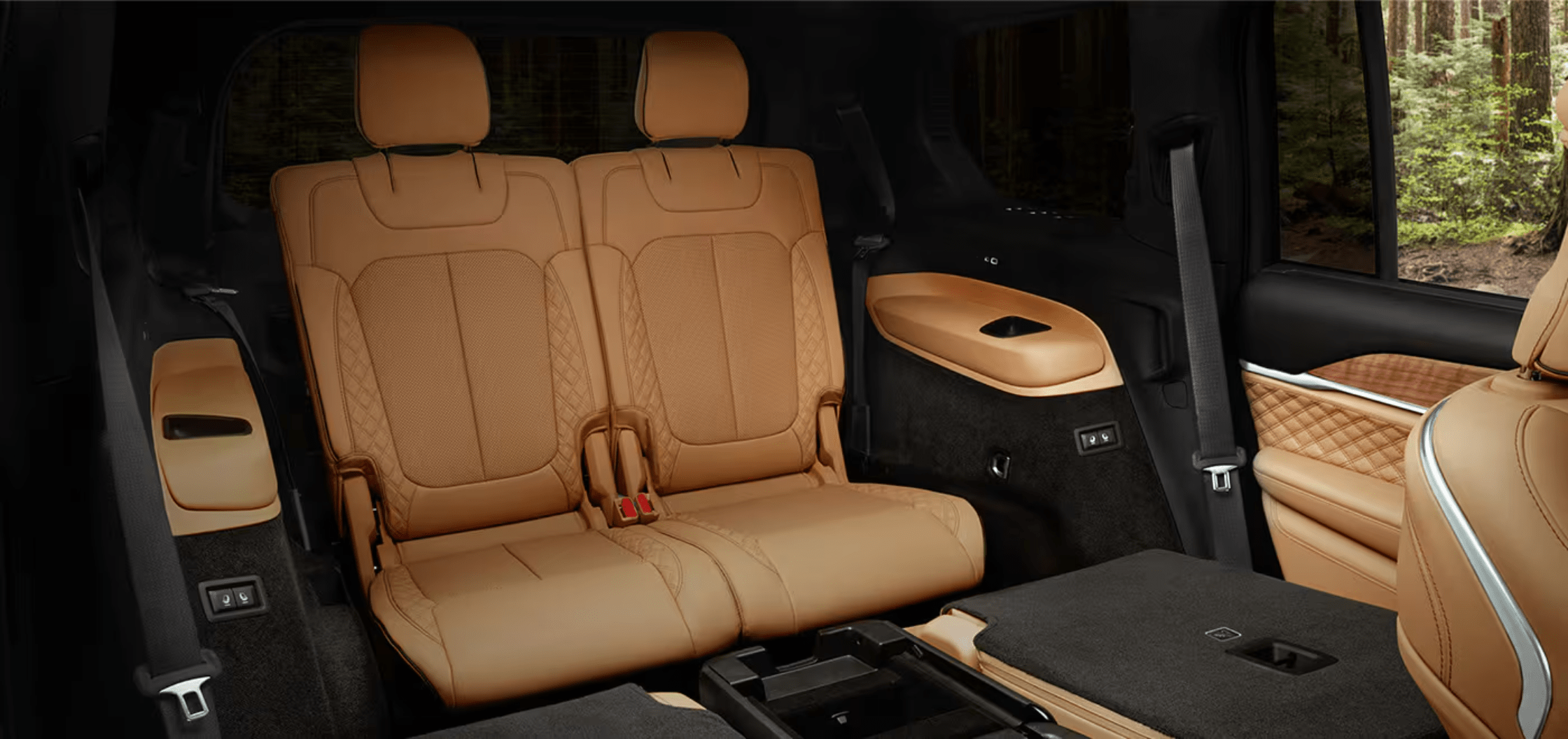 Two tan leather seats in a vehicle interior with a view of a forest through the window.