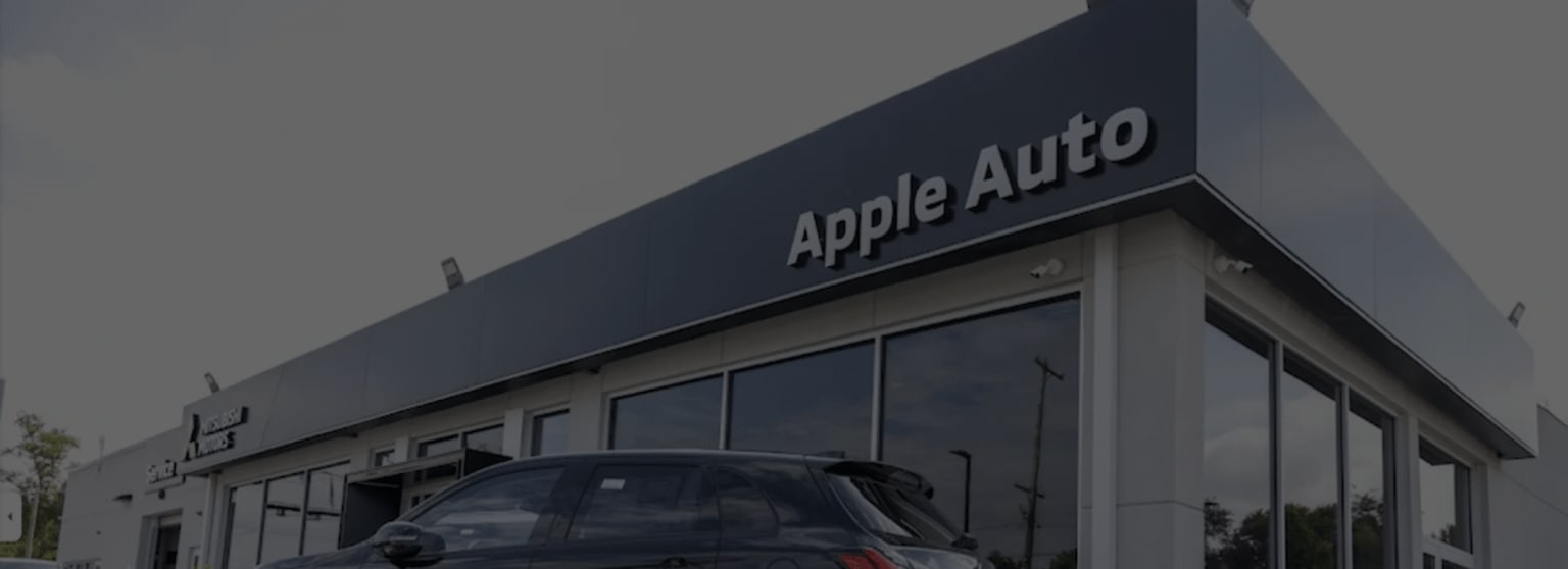 a car parked in front of a apple auto showroom in a parking lot in front of a building