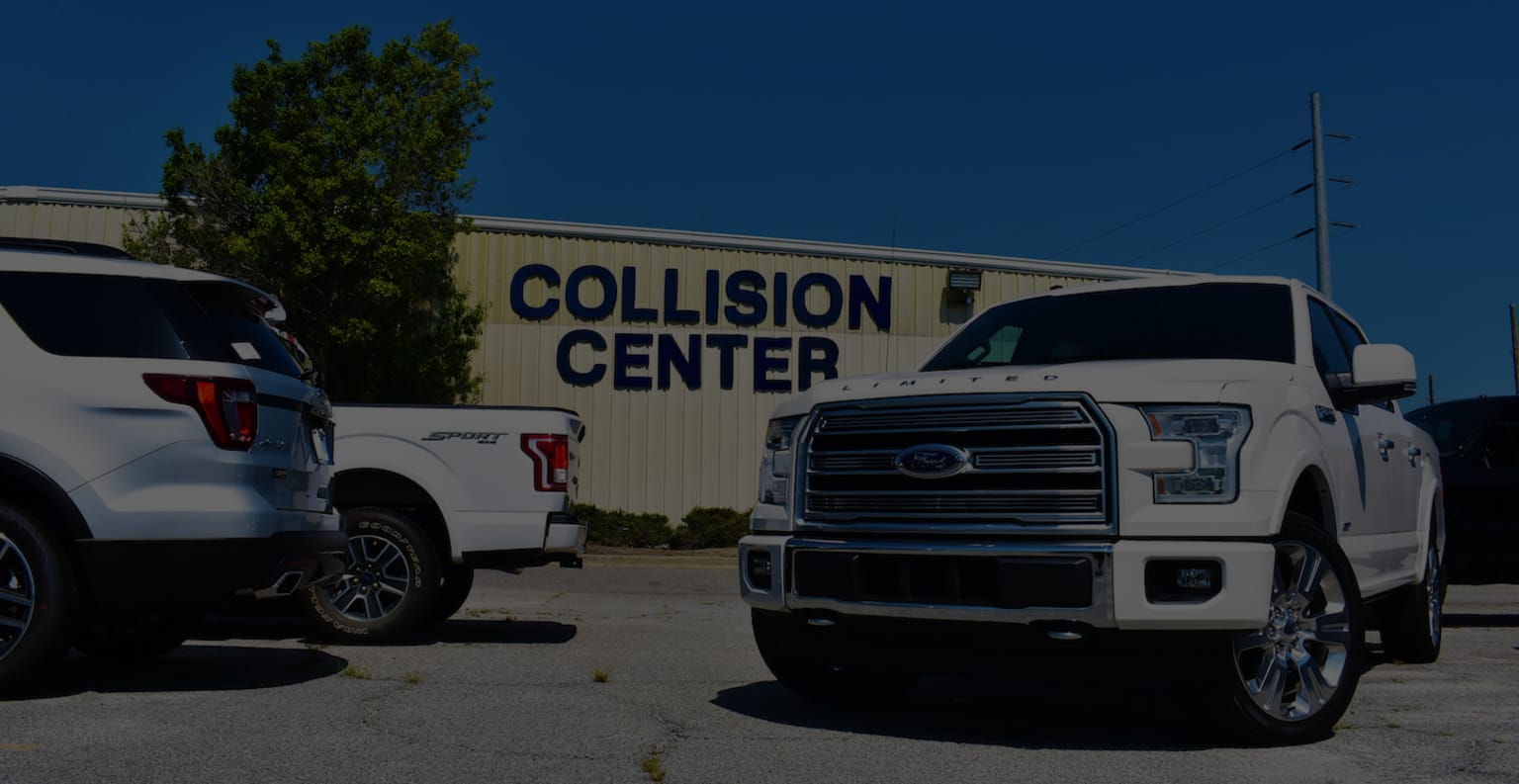 two white trucks are parked in front of a collision center sign and a building with a sign that says collision center