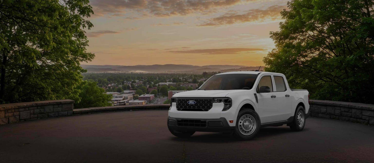 A white pickup truck overlooking a town and rolling hills at sunset.