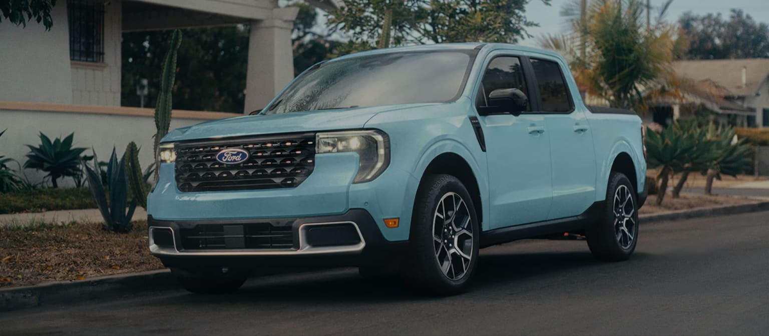 A light blue pickup truck is parked on a suburban street in front of a house with lush greenery.