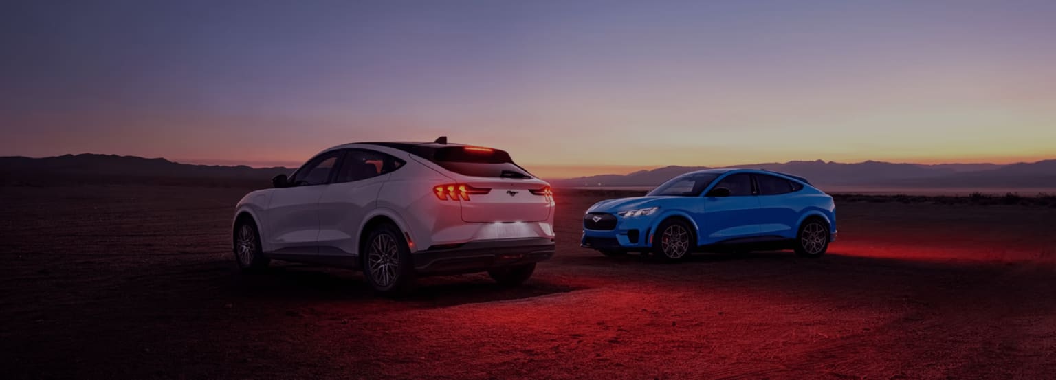 Two SUVs, one white and one blue, are parked on a dusty plain under a twilight sky with distant mountains.