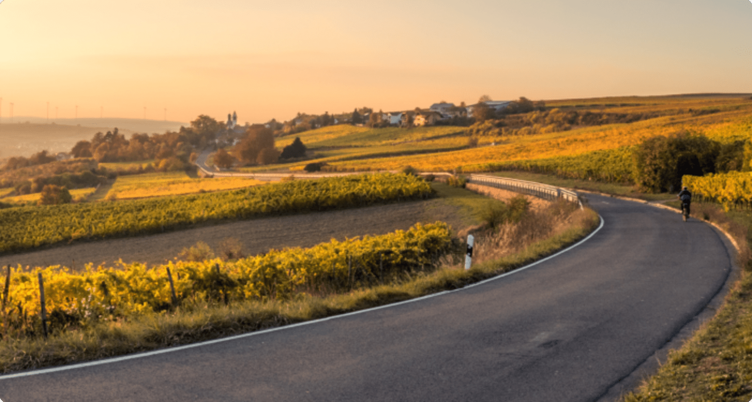 a person riding a bike down a curvy road in a rural area with fields and hills in the background