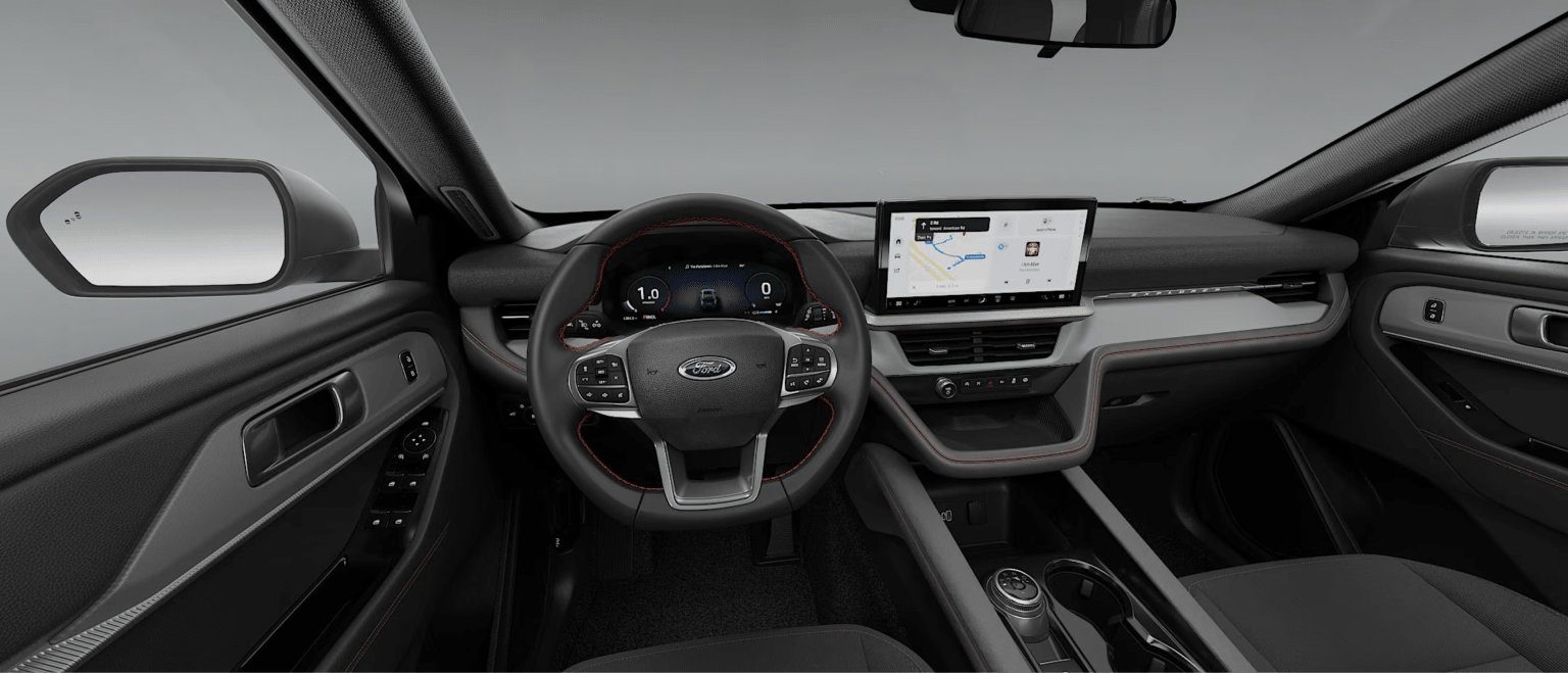 Modern car interior with leather-wrapped steering wheel, digital dashboard, wide infotainment screen, and grey dashboard.