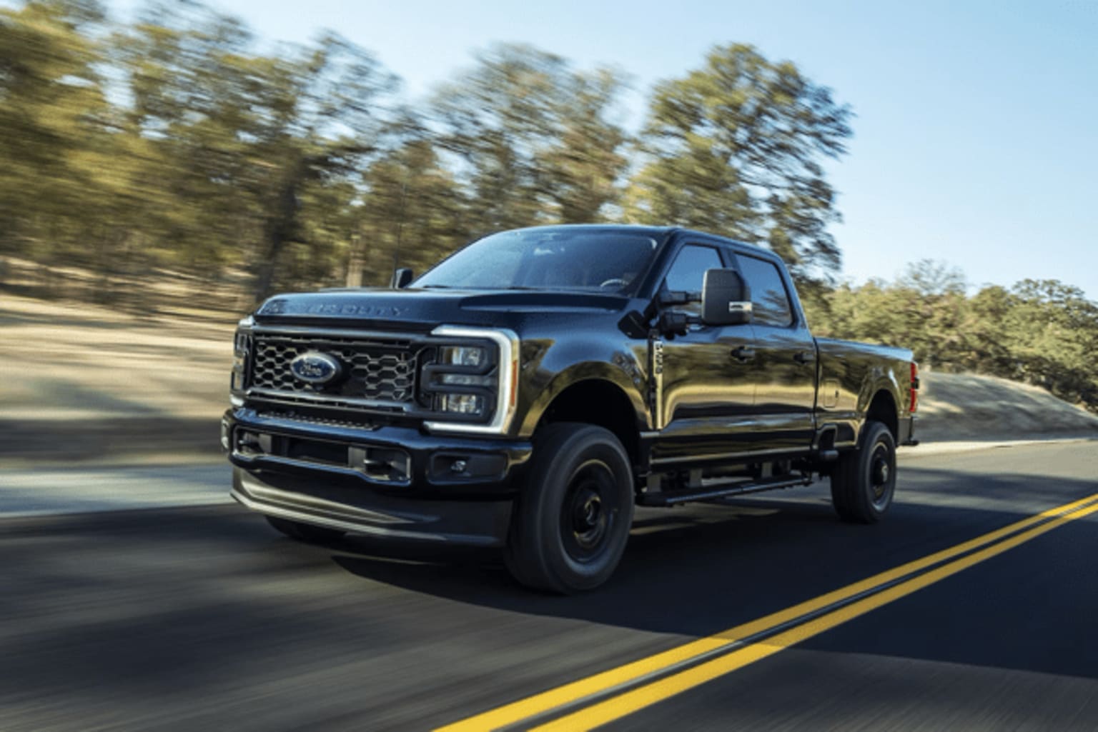 A black pickup truck driving on a winding road surrounded by forested scenery on a sunny day.