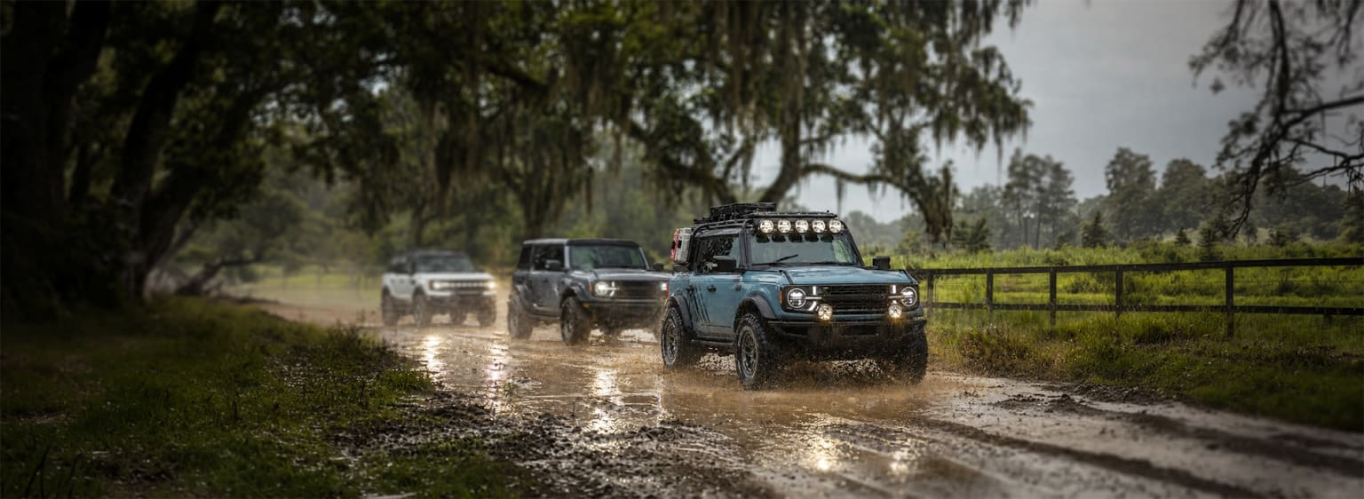 Off-road vehicles on muddy dirt road with greenery and trees.