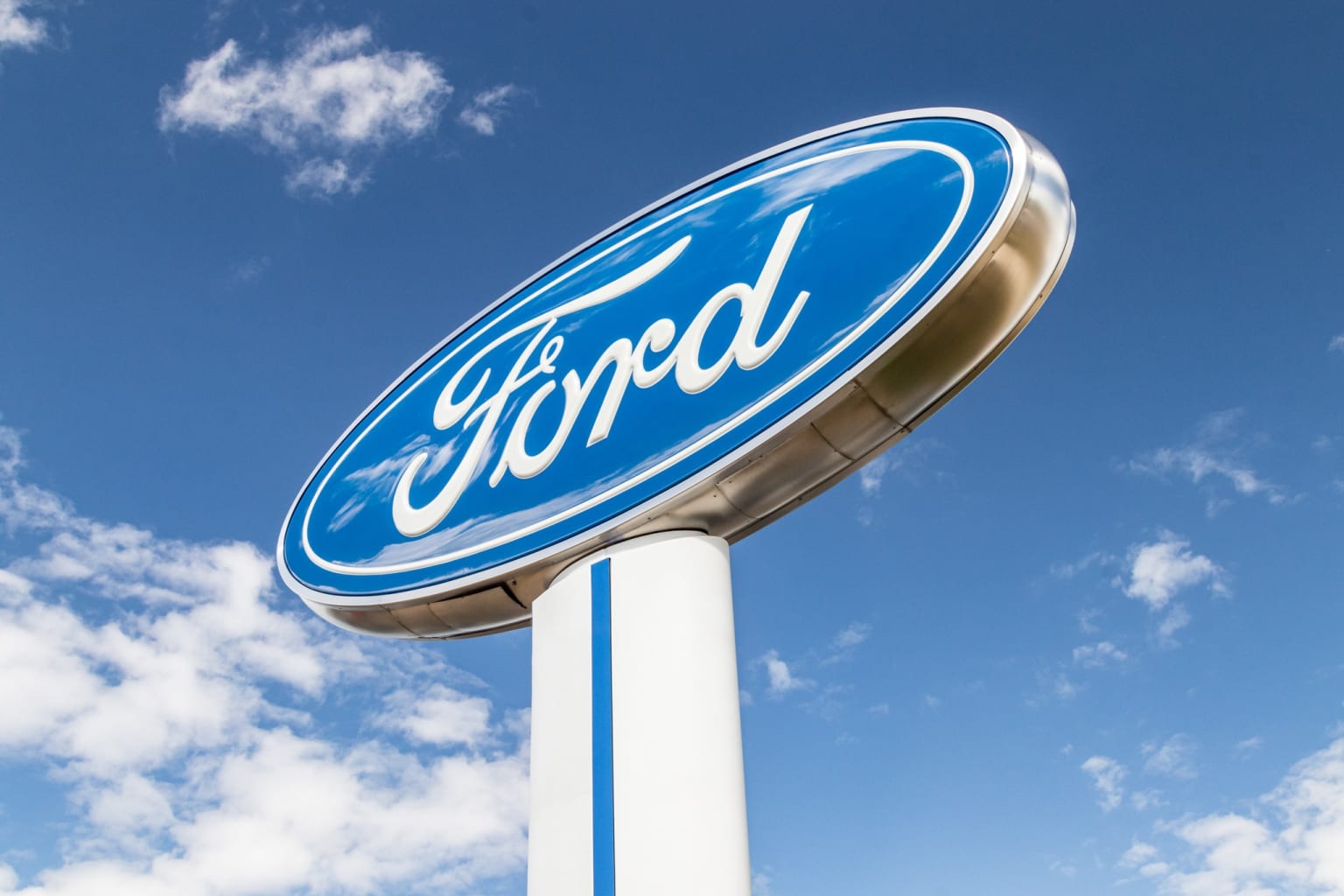 a blue and white ford sign under a blue sky with white clouds and blue sky in the back ground