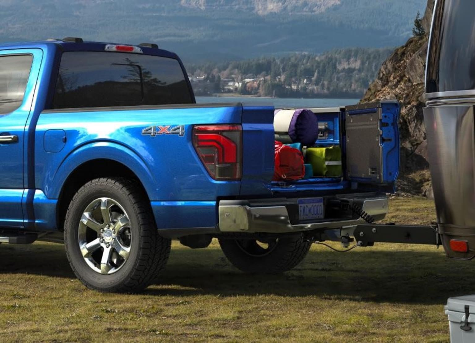 Blue pickup truck on grass with mountainous landscape.