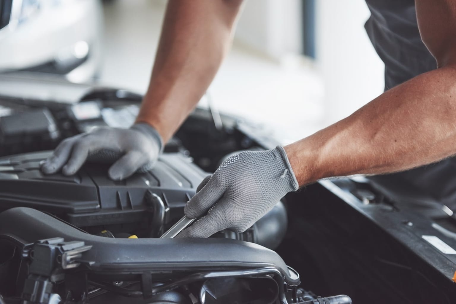 a man working on a car's engine in a garage with a glove on his hand and a wrench in his other hand