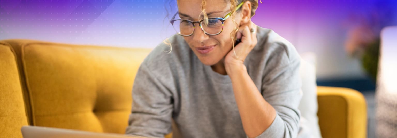 A person wearing glasses and a gray sweater appears to be smiling and gesturing with their hands against a vibrant purple and orange background.