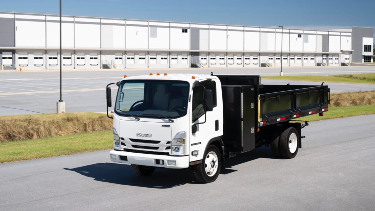 A white dump truck parked in front of a large white industrial building.