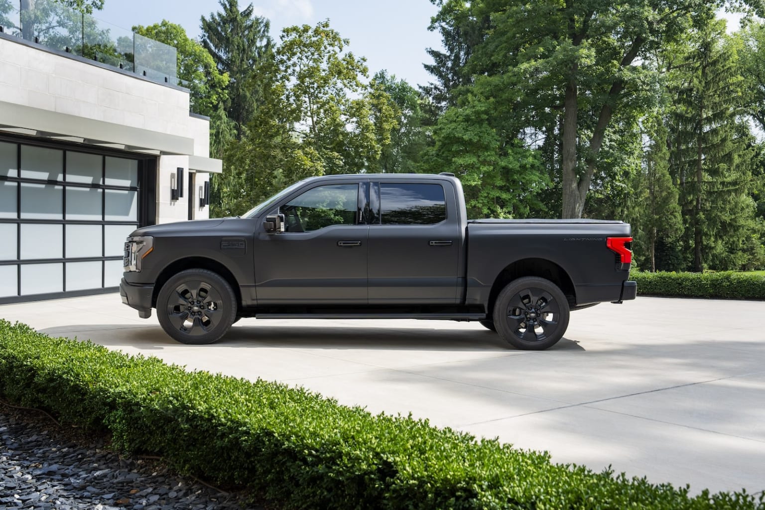 a black truck parked in front of a house with a driveway in front of it and trees in the background