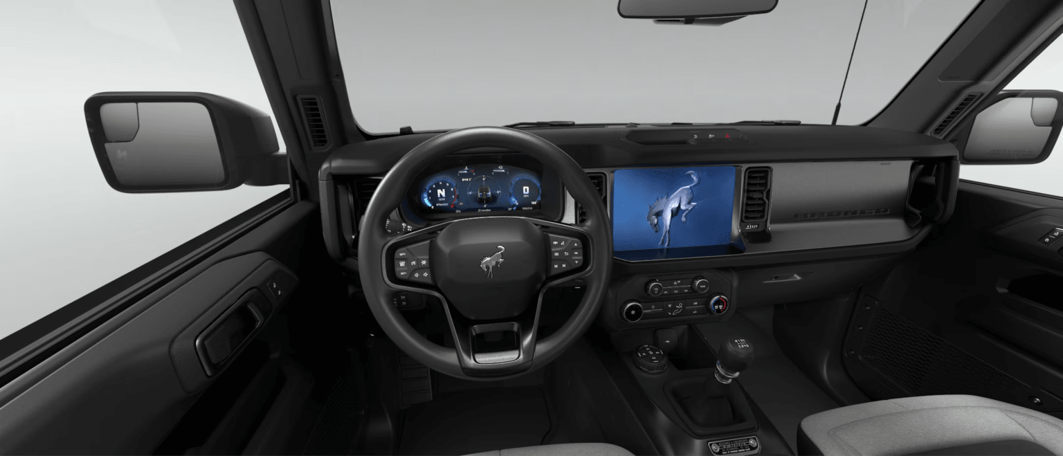 Interior of a car with a steering wheel and dashboard, background is a plain white wall.