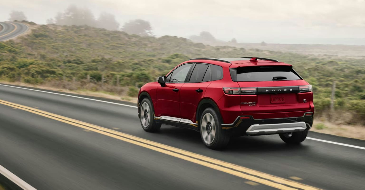 A red SUV driving on a winding road with a misty, hilly landscape in the background.