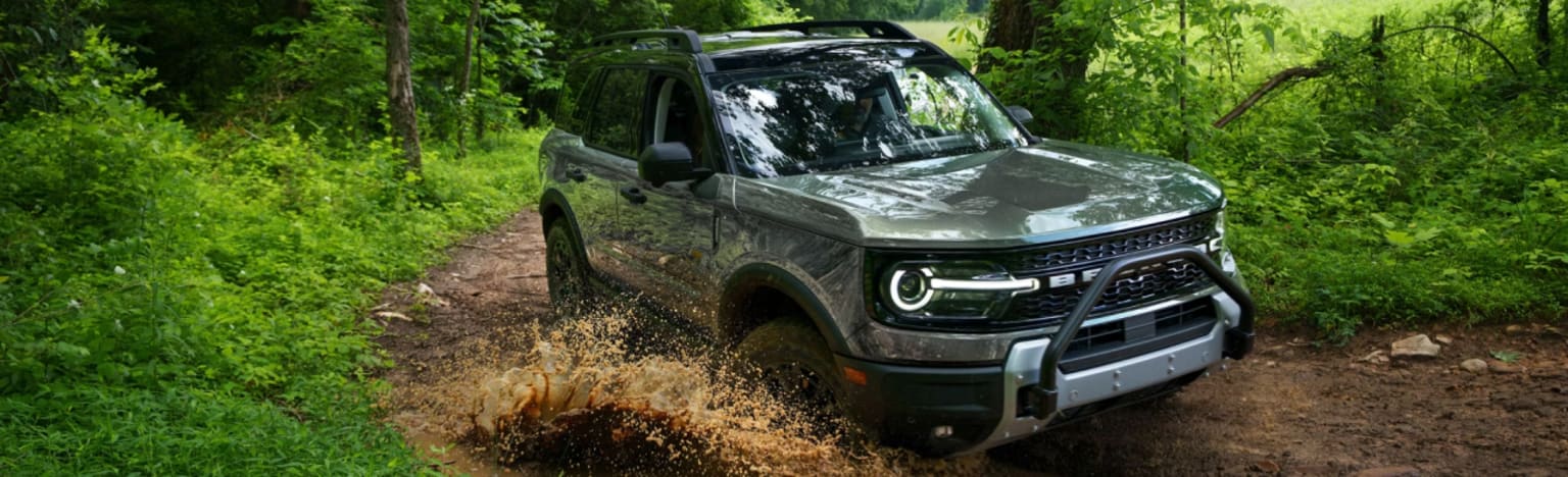 Gray SUV off-roading through muddy trail with green trees and foliage.