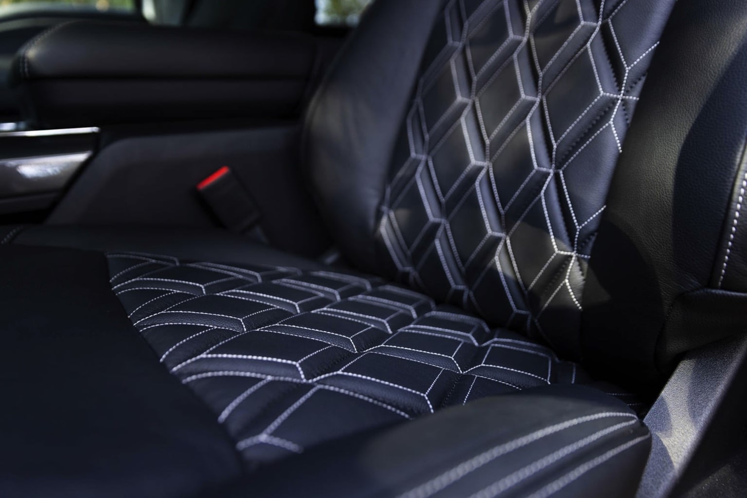 Interior of a vehicle with patterned upholstery seats featuring a geometric, diamond-shaped design in shades of black and gray, creating a visually striking and textured appearance.