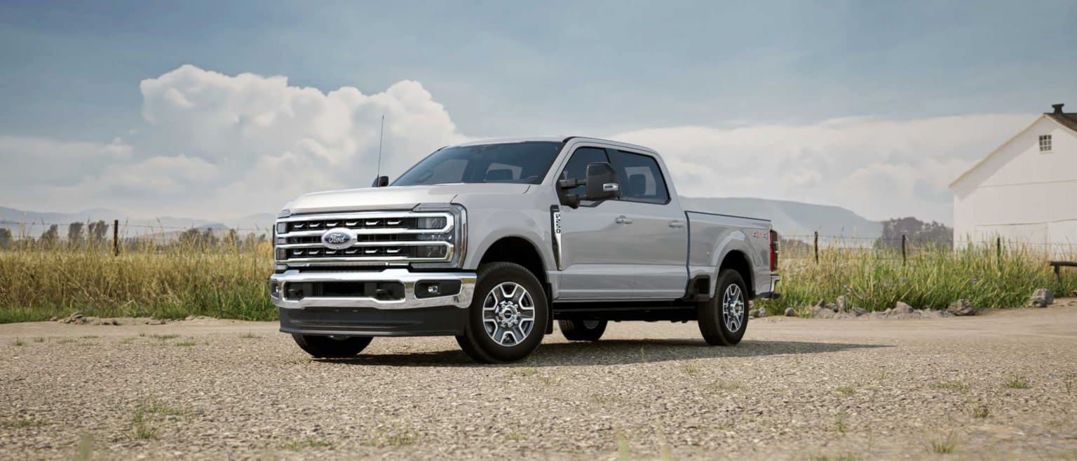 A rugged, silver pickup truck stands in a grassy field against a backdrop of cloudy skies.